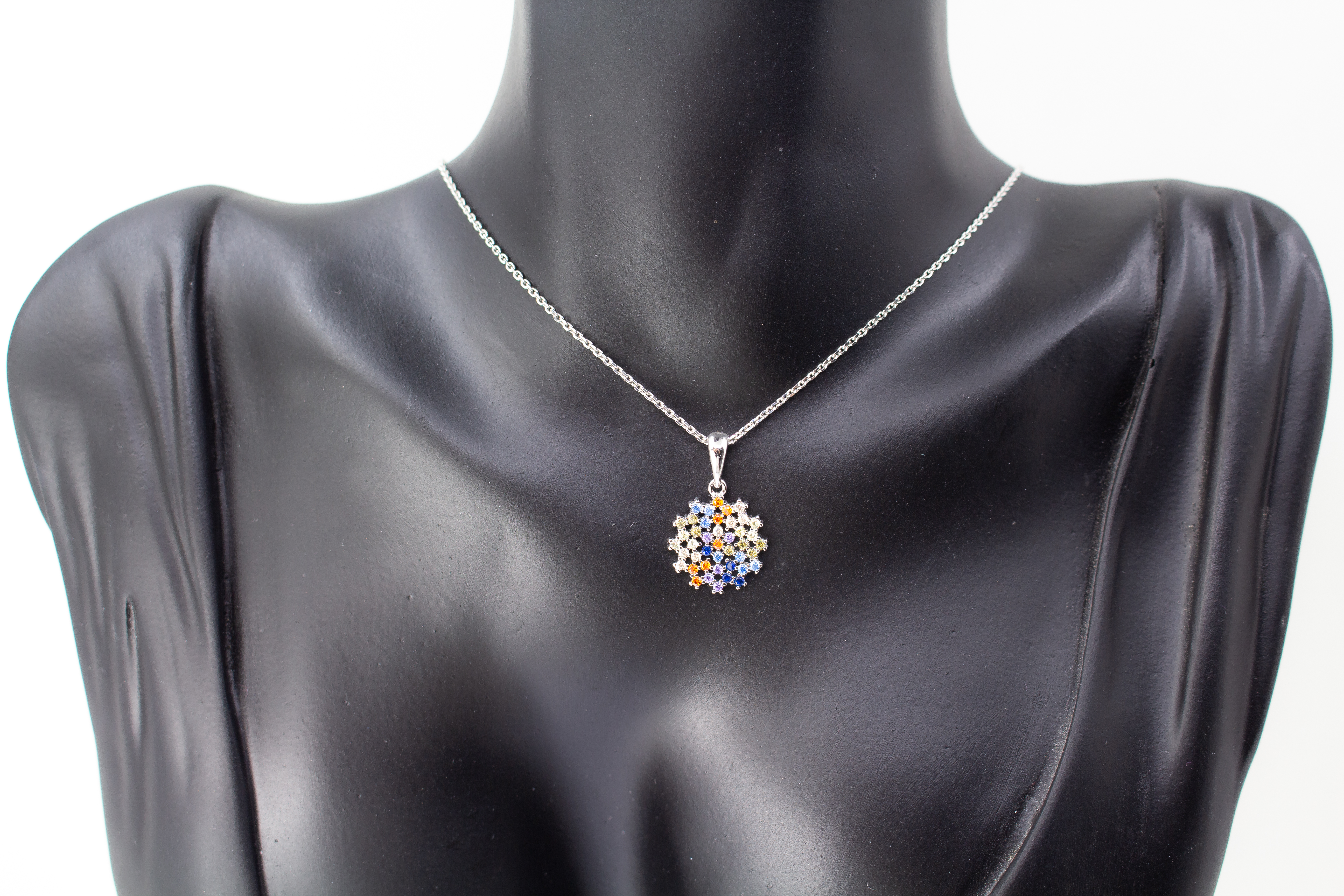 Eine feine Halskette aus rhodiniertem 925er Sterlingsilber von der Goldschmiede Regina Kraus, schräg auf weißem Hintergrund liegend. Der runde Anhänger ist filigran wie ein Mandala oder eine Blüte gestaltet und dicht mit kleinen, bunt funkelnden Zirkonia-