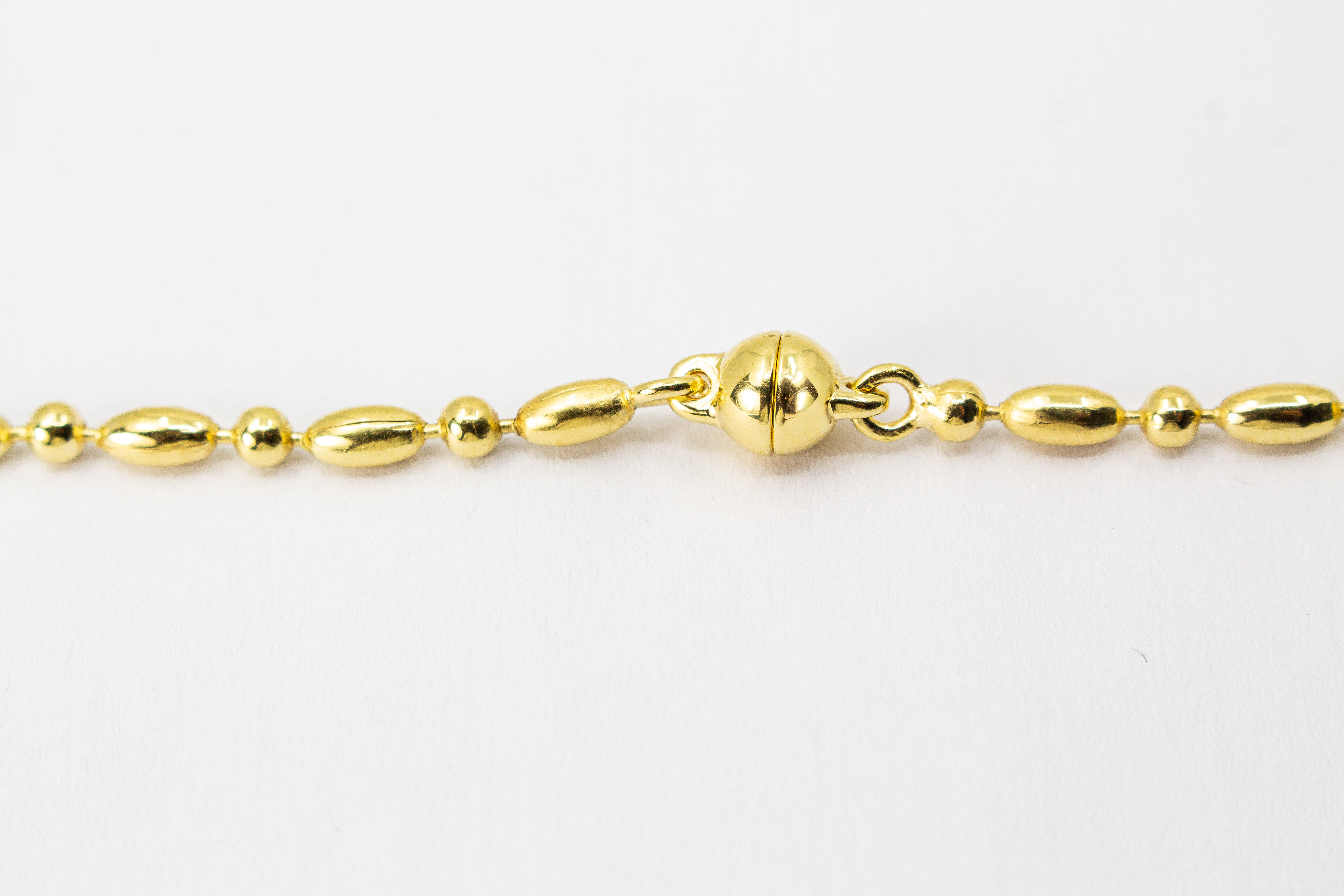 Elegantes, hochwertig vergoldetes Collier aus 925er Sterlingsilber mit einer 20 Mikron Vergoldung, gestaltet in einem rhythmischen Wechsel aus polierten Oliven- und Kugel-Elementen auf hellem Hintergrund, aus dem Schmuck-Onlineshop der Goldschmiede Regina