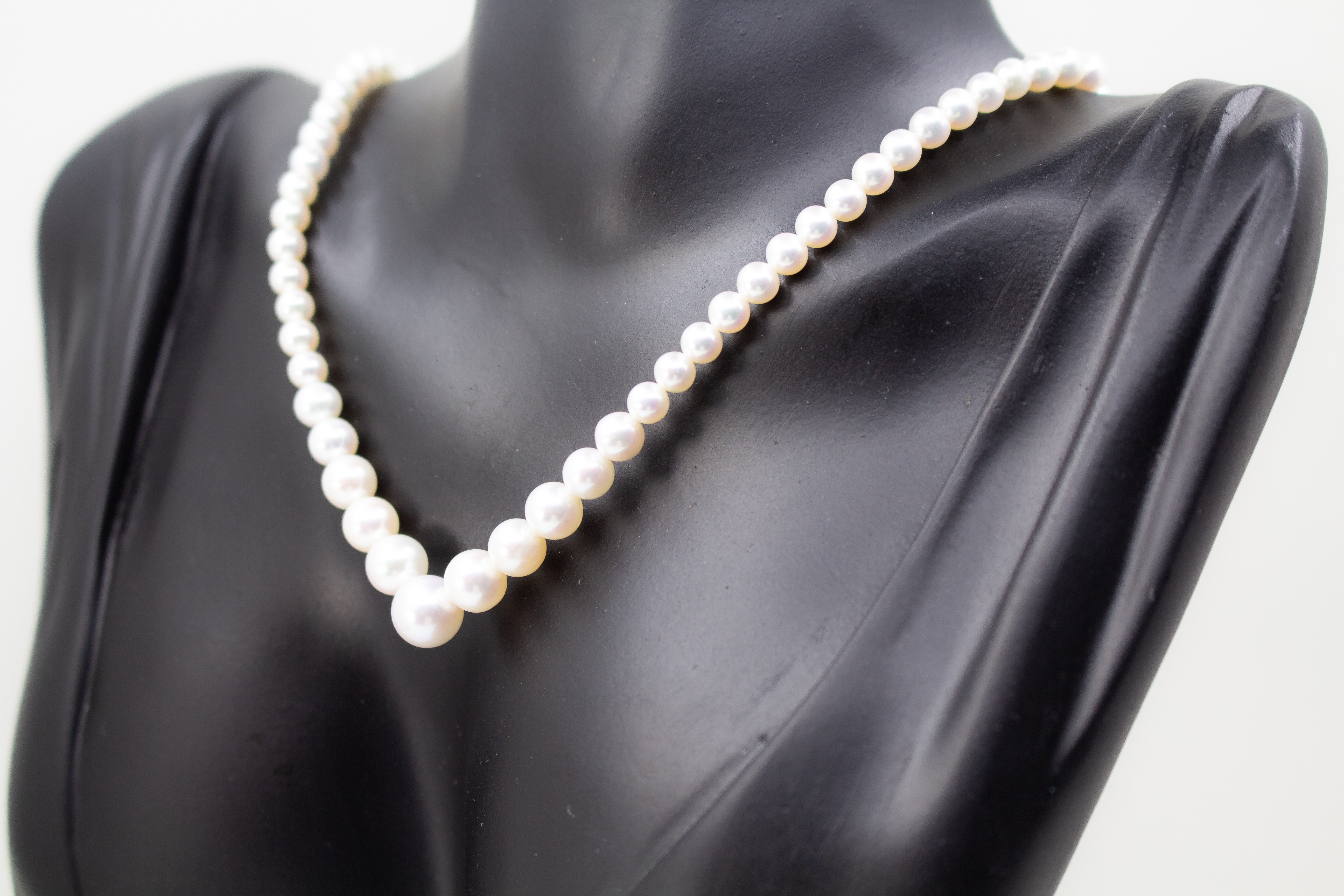 Eine klassische Süßwasserzuchtperlenkette von der Goldschmiede Regina Kraus, elegant geschwungen auf weißem Hintergrund ausgelegt. Die runden Perlen weisen einen zarten, cremeweißen Lüster auf und sind im harmonischen Verlauf angeordnet, wobei die größte
