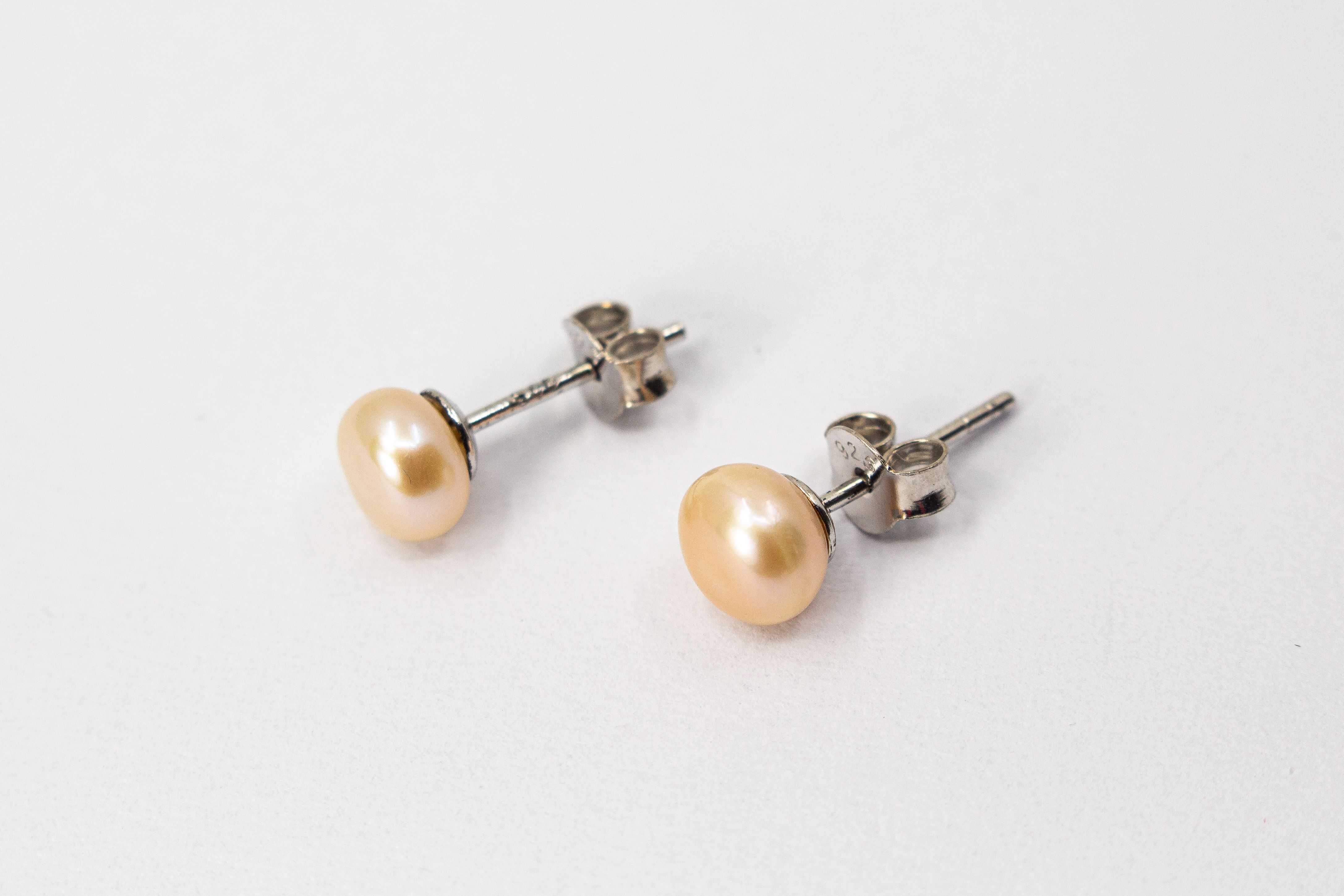 Ein Paar klassische Damen-Ohrstecker aus poliertem 925 Sterlingsilber mit je einer runden, lachsfarbenen Süßwasserzuchtperle, präsentiert von der Goldschmiede Regina Kraus.