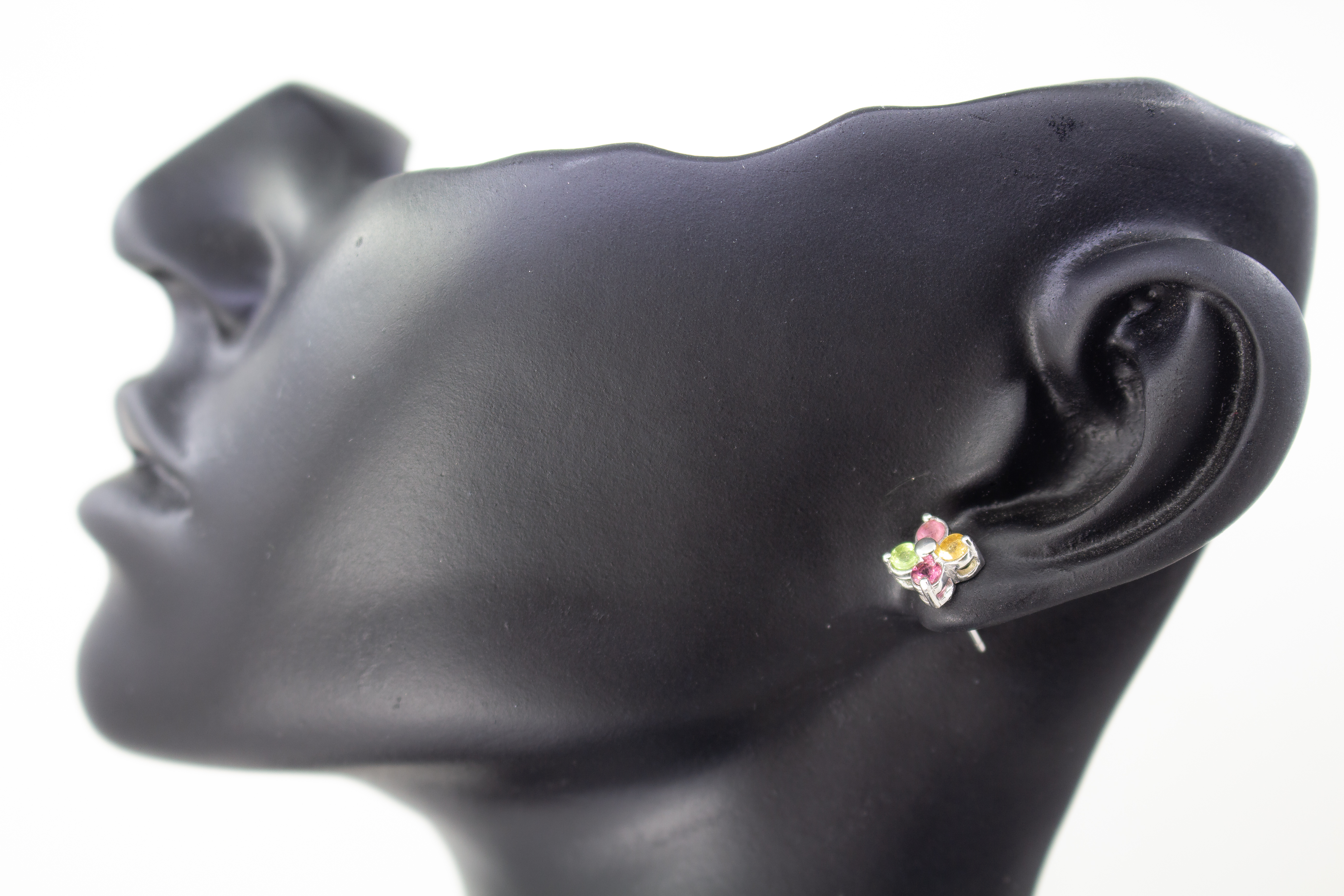 Die filigranen Silber-Ohrstecker „Elfenblüte“ aus der Goldschmiede Regina Kraus an einem transparenten Halter. Die Stecker aus rhodiniertem 925er Sterlingsilber zeigen eine zarte Blütenform, besetzt mit vier bunten Turmalinen in Rosé, Grün und Gelb um ei