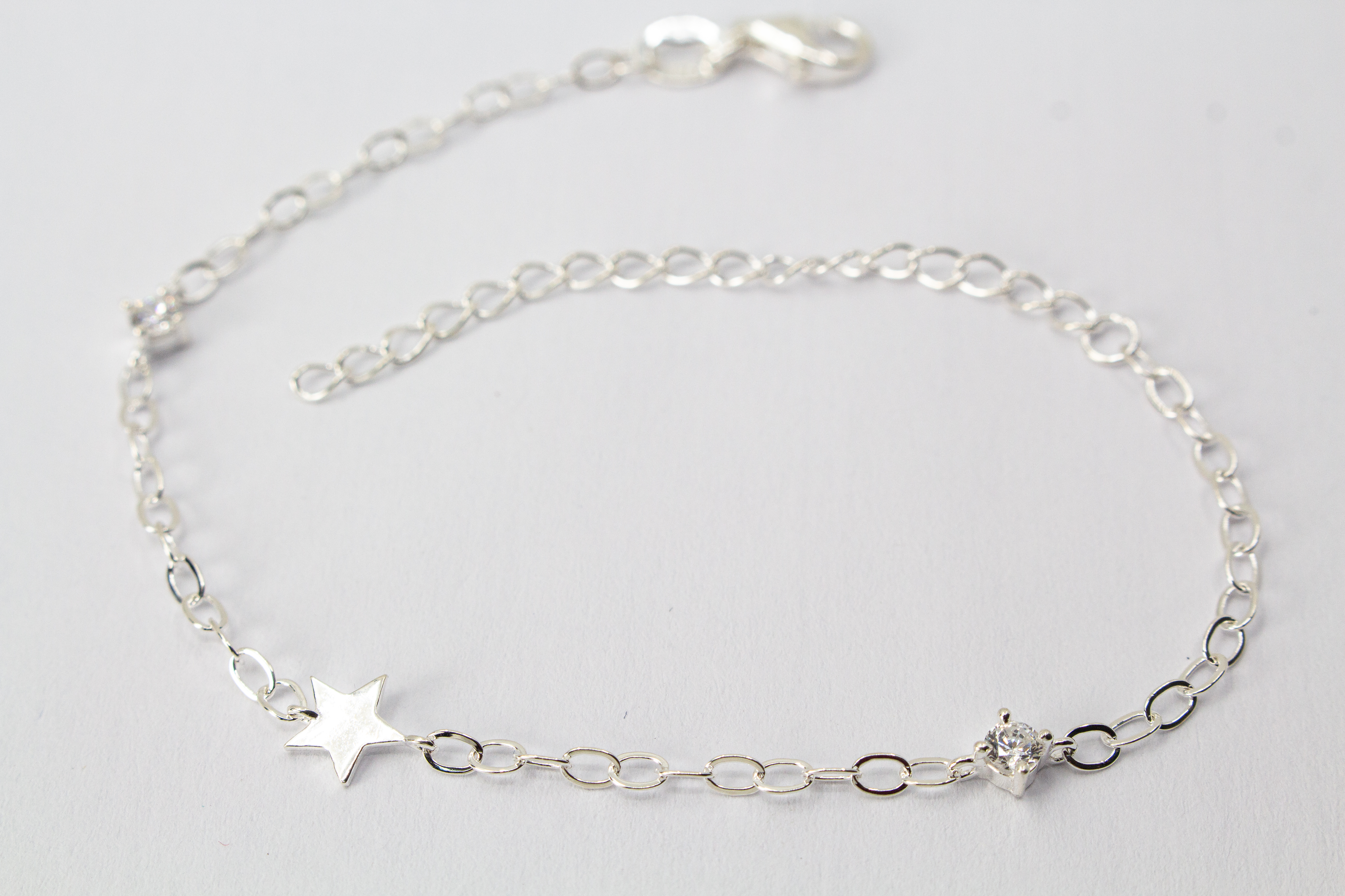 Filigranes Gliederarmband aus hochglanzpoliertem 925er Sterlingsilber mit einem flachen Stern-Anhänger und einem quadratisch gefassten Zirkonia-Kristall.