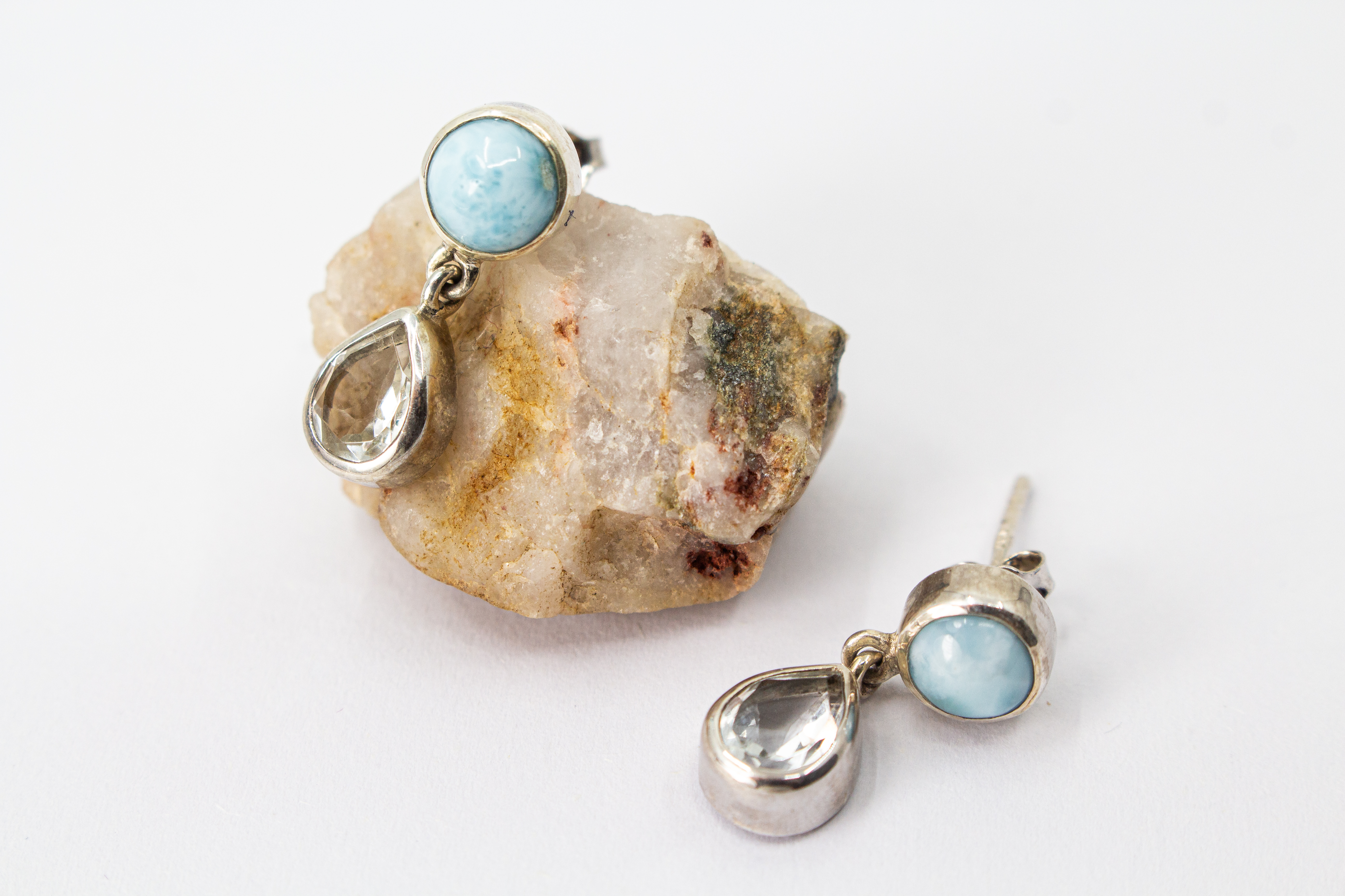 Filigrane, zweiteilige Ohrstecker aus 925 Sterling Silber mit einer runden, hellblauen Larimar-Kugel und einem frei beweglich hängenden, klaren Bergkristall-Tropfen im Onlineshop der Goldschmiede Regina Kraus.