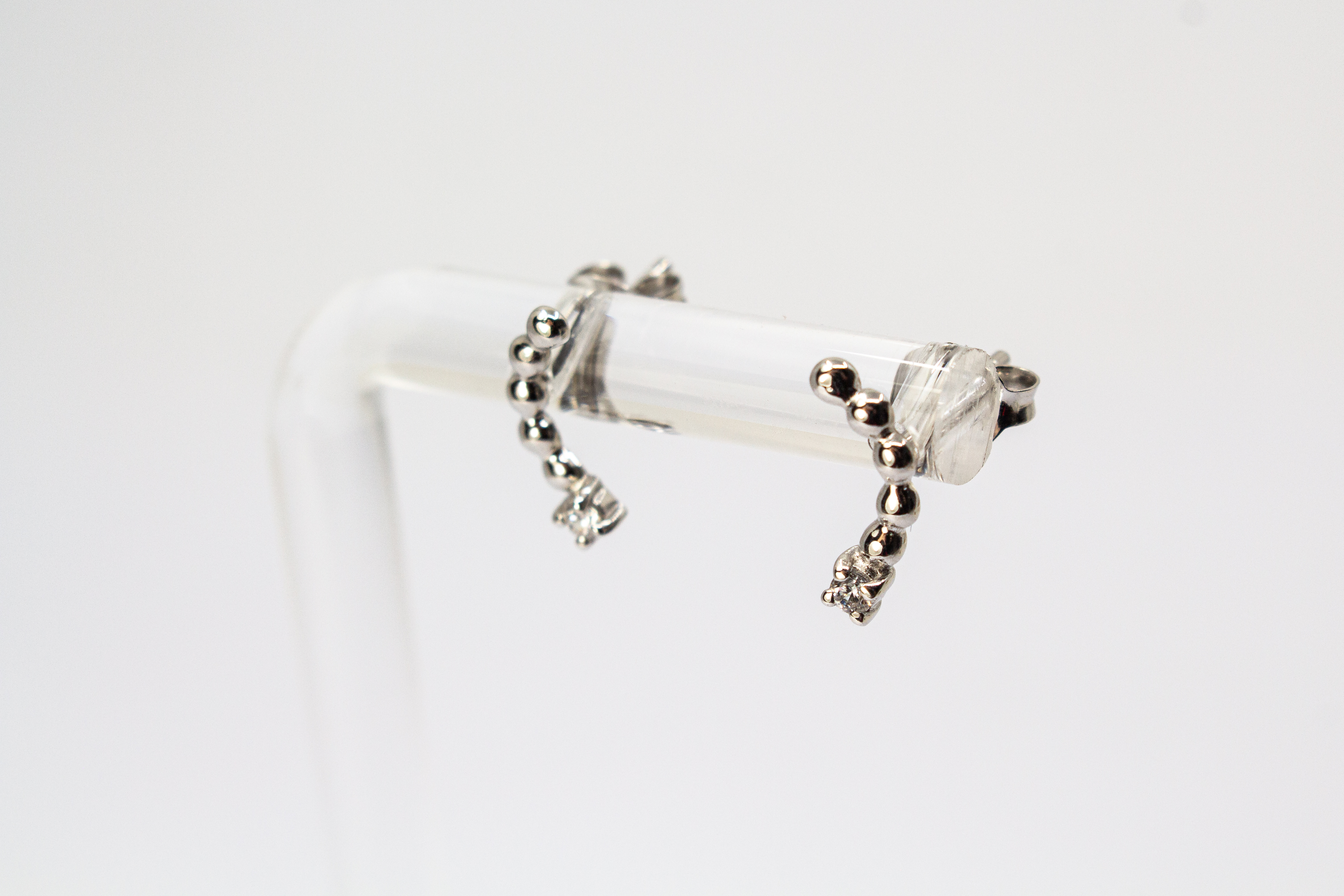 Moderne Ohrstecker aus rhodiniertem 925er Silber mit einem geschwungenen Bogen aus feinen Silberkugeln und funkelnden Zirkoniasteinen im Onlineshop von Goldschmiede Regina Kraus.