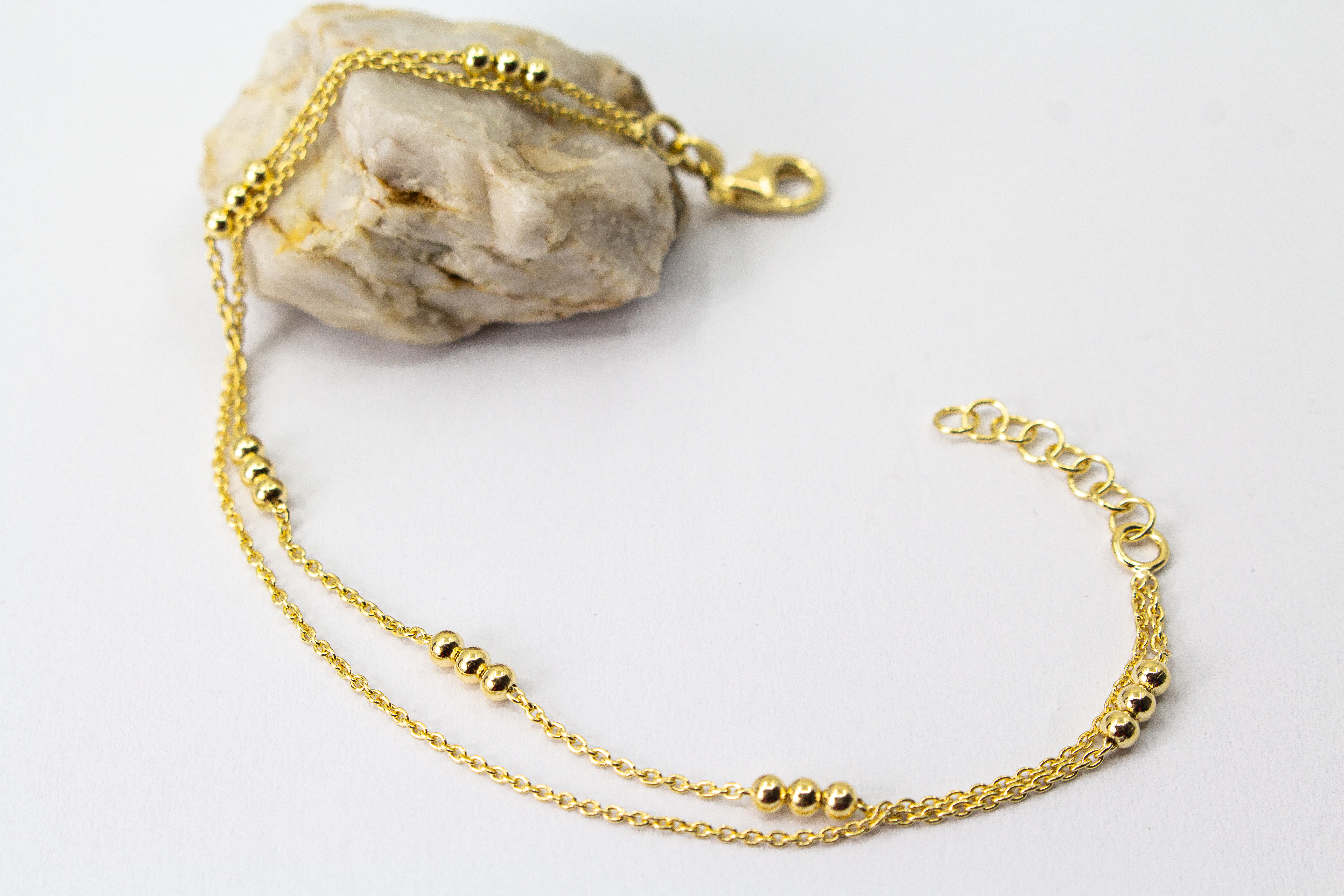 Zartes, zweireihiges Armband aus vergoldetem 925er Silber mit kleinen Goldkugeln, die in Dreiergruppen auf zwei feinen Ankerketten angeordnet sind.