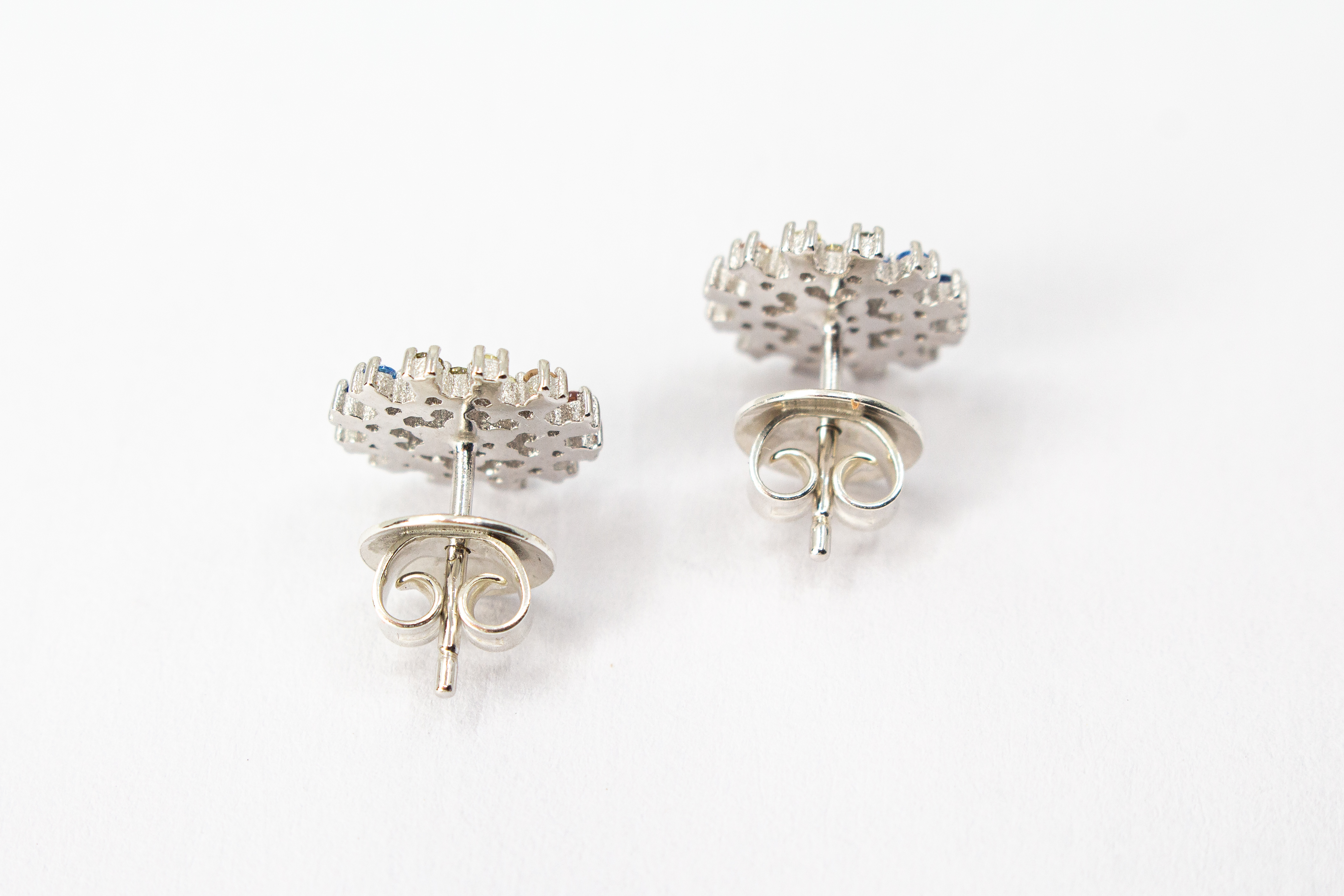 Die filigranen 925er Silber-Ohrstecker „Fleur de Lumière“ aus der Goldschmiede Regina Kraus, präsentiert auf einem transparenten Schmuckständer. Das florale Design erinnert an eine funkelnde Lichtblume und ist kunstvoll mit kleinen, bunt strahlenden Zirk