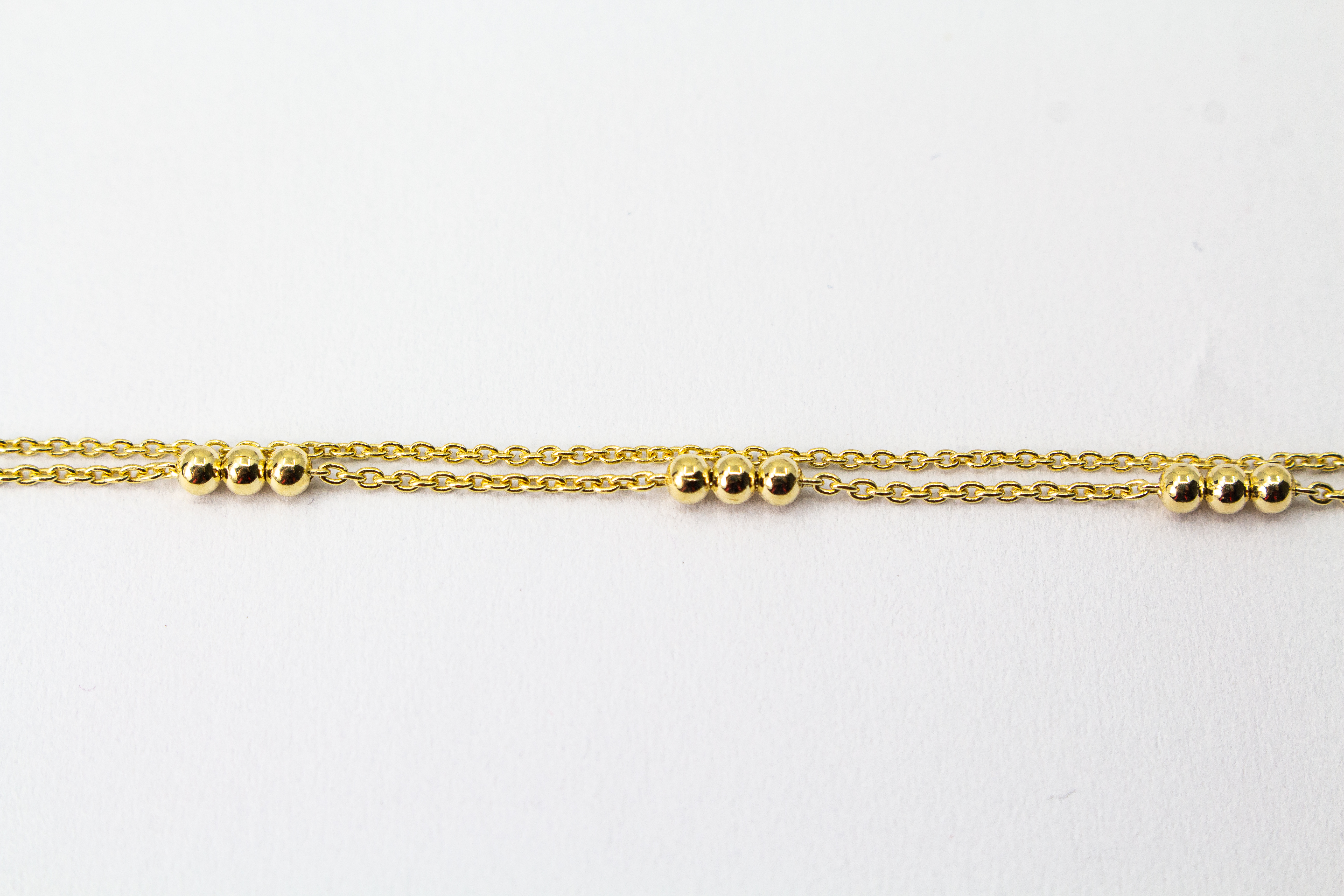 Zartes, zweireihiges Armband aus vergoldetem 925er Silber mit kleinen Goldkugeln, die in Dreiergruppen auf zwei feinen Ankerketten angeordnet sind.