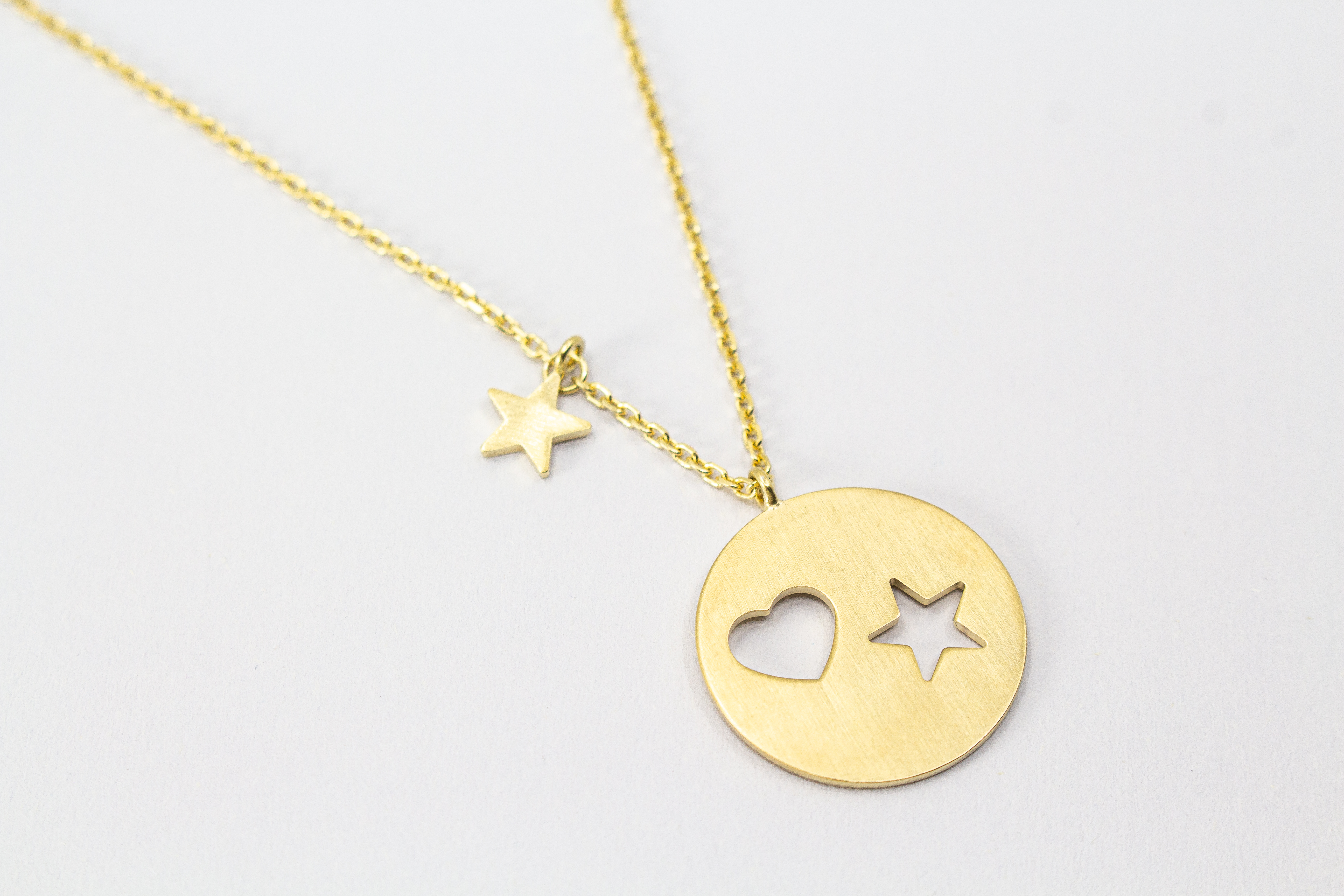 Collier „Sternenliebe“ aus vergoldetem 925er Sterlingsilber mit rundem Anhänger, Herz- und Sternmotiv sowie zusätzlichem Sternanhänger.