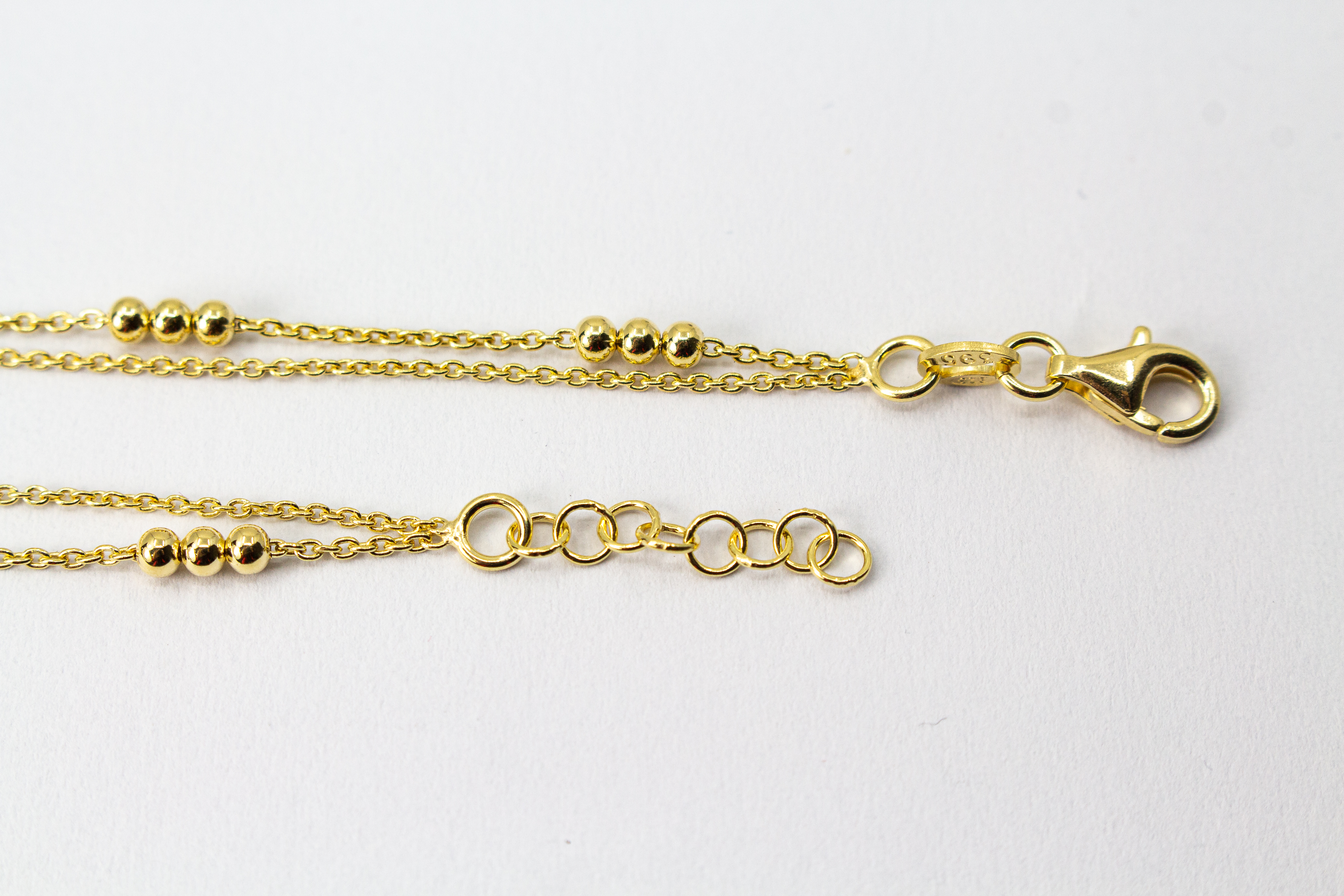 Zartes, zweireihiges Armband aus vergoldetem 925er Silber mit kleinen Goldkugeln, die in Dreiergruppen auf zwei feinen Ankerketten angeordnet sind.