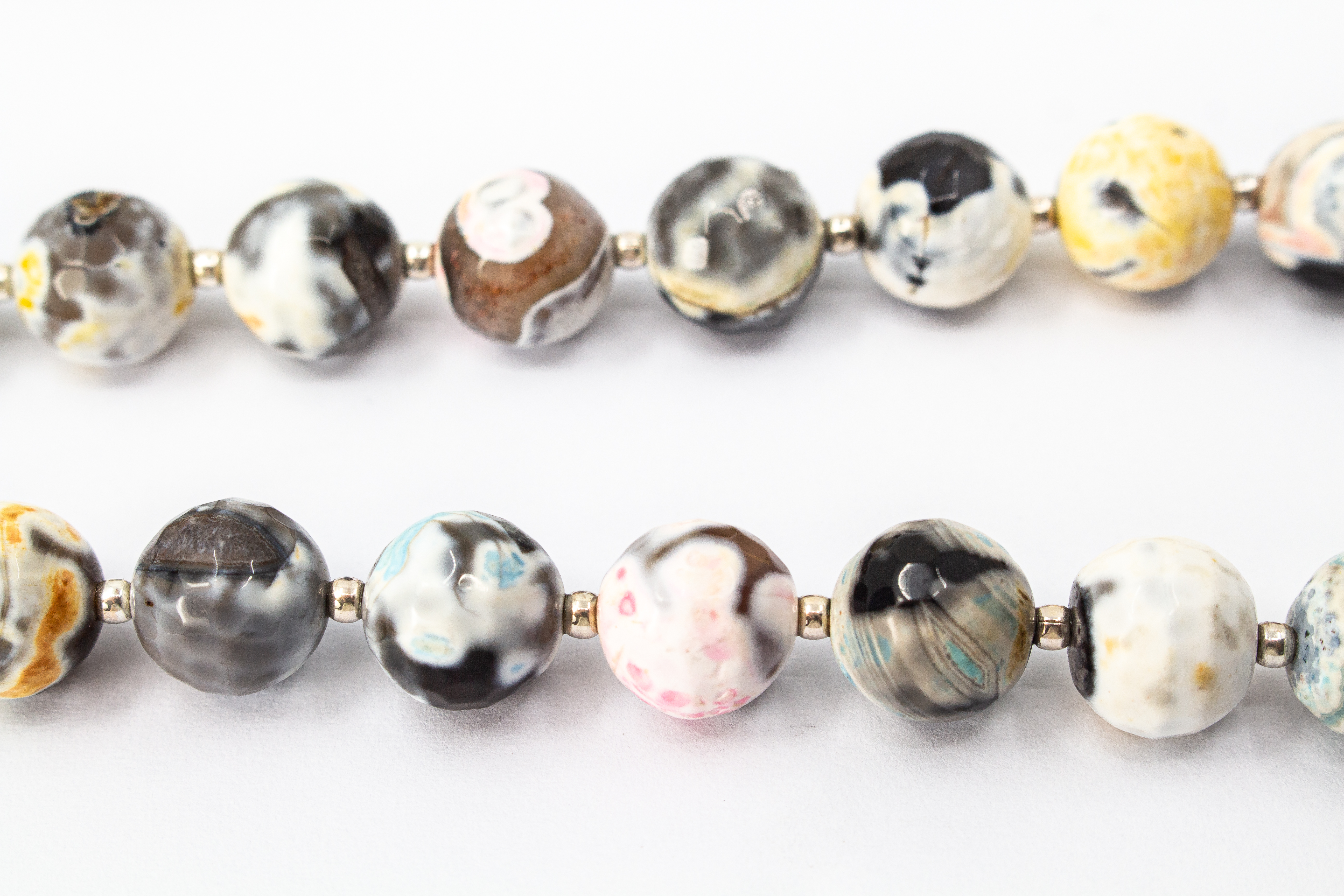 Ein handgefertigtes Collier aus bunt gemusterten, runden Feuerachat-Perlen mit kleinen silbernen Zwischenelementen und Magnetschließe