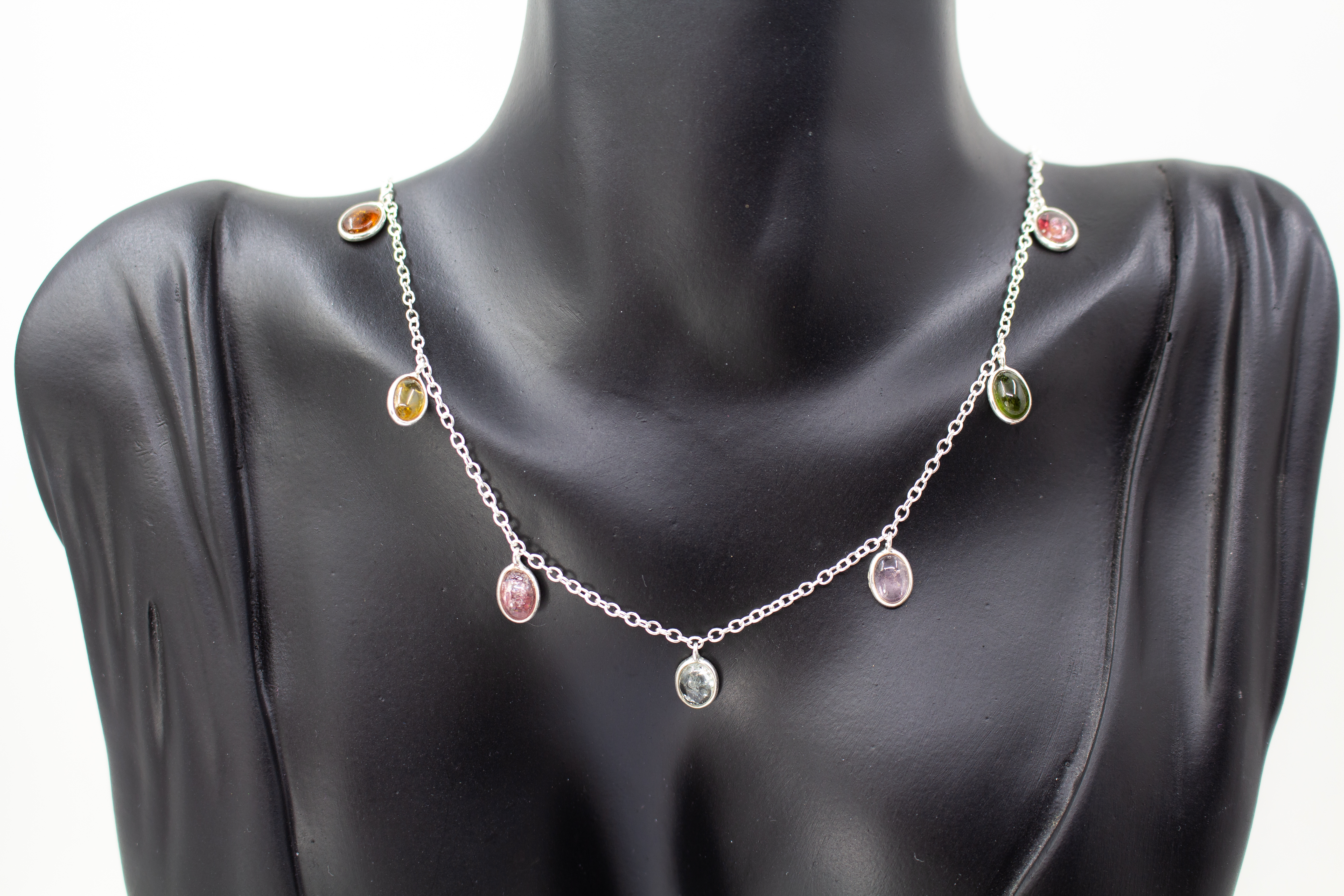 Die filigrane 925er Silber-Halskette „Kaleidoskop der Natur“ aus der Goldschmiede Regina Kraus, spiralförmig auf hellem Grund arrangiert. Das Design besticht durch ein buntes Farbspiel aus elf facettierten, ovalen Turmalinen in zarten Silberfassungen, die