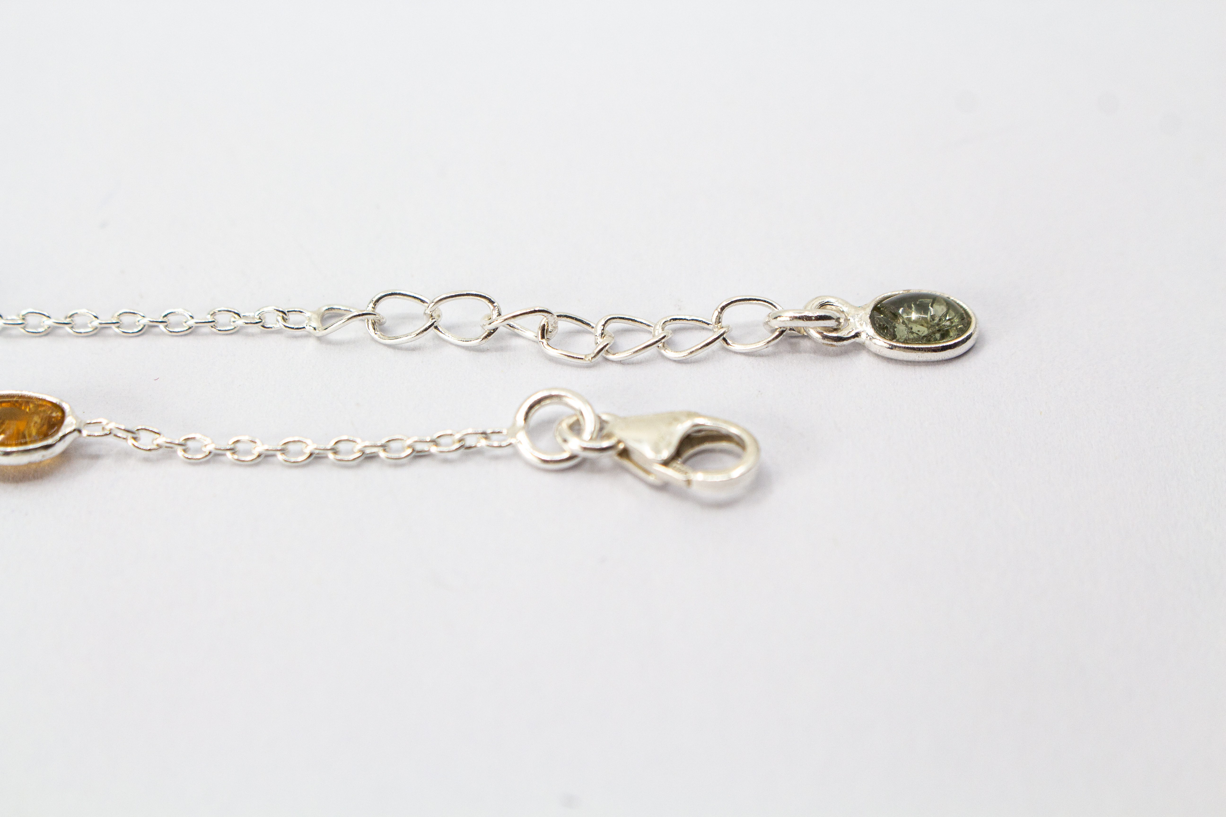 Das filigrane Silber-Armband „Indian Summer“ aus der Goldschmiede Regina Kraus, flach auf weißem Untergrund arrangiert. Die feine Kette aus rhodiniertem 925er Sterlingsilber verbindet fünf ovale Turmalin-Cabochons in den warmen Farben Weinrot, Moosgrün, R
