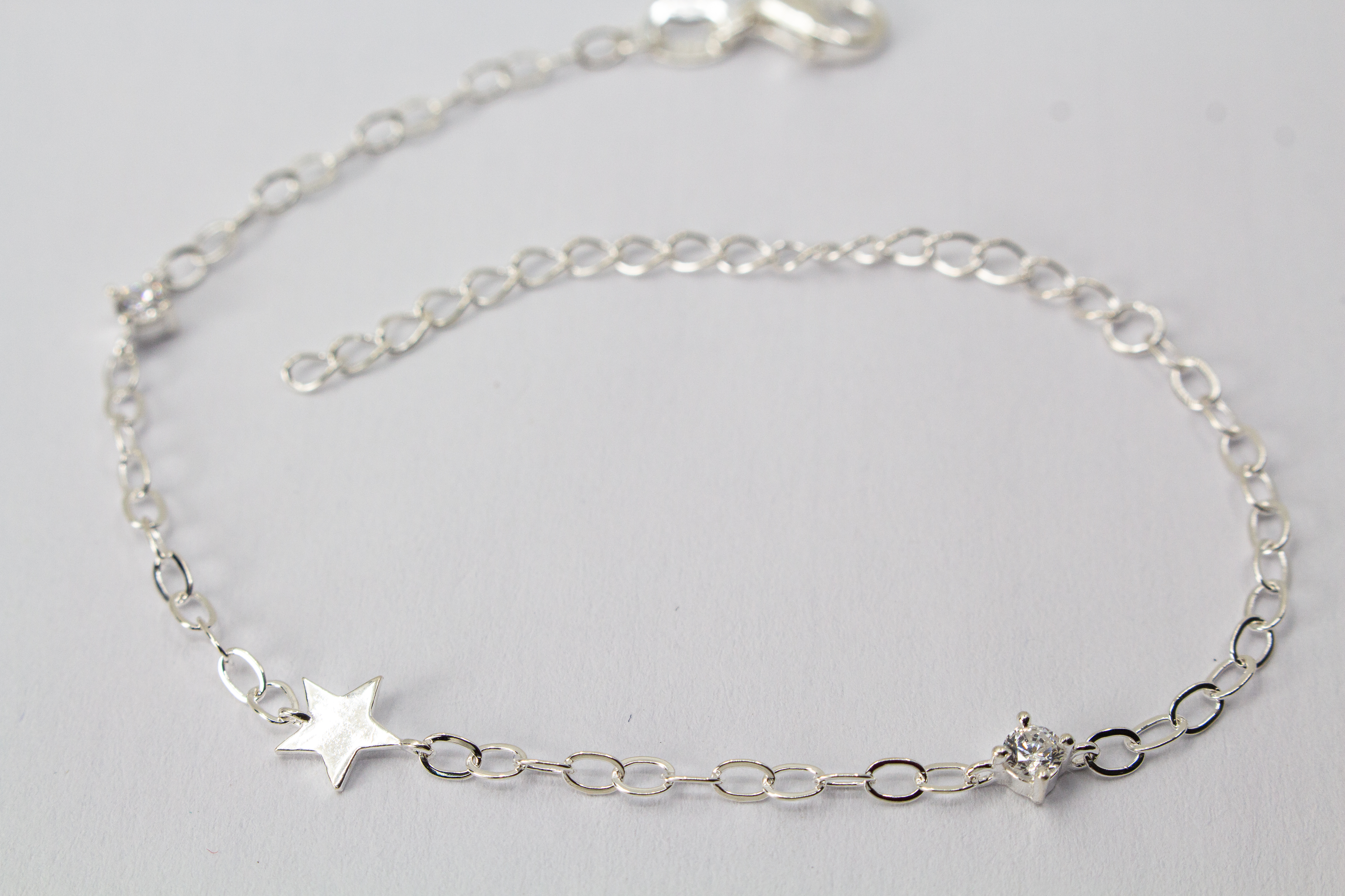 Filigranes Gliederarmband aus hochglanzpoliertem 925er Sterlingsilber mit einem flachen Stern-Anhänger und einem quadratisch gefassten Zirkonia-Kristall.