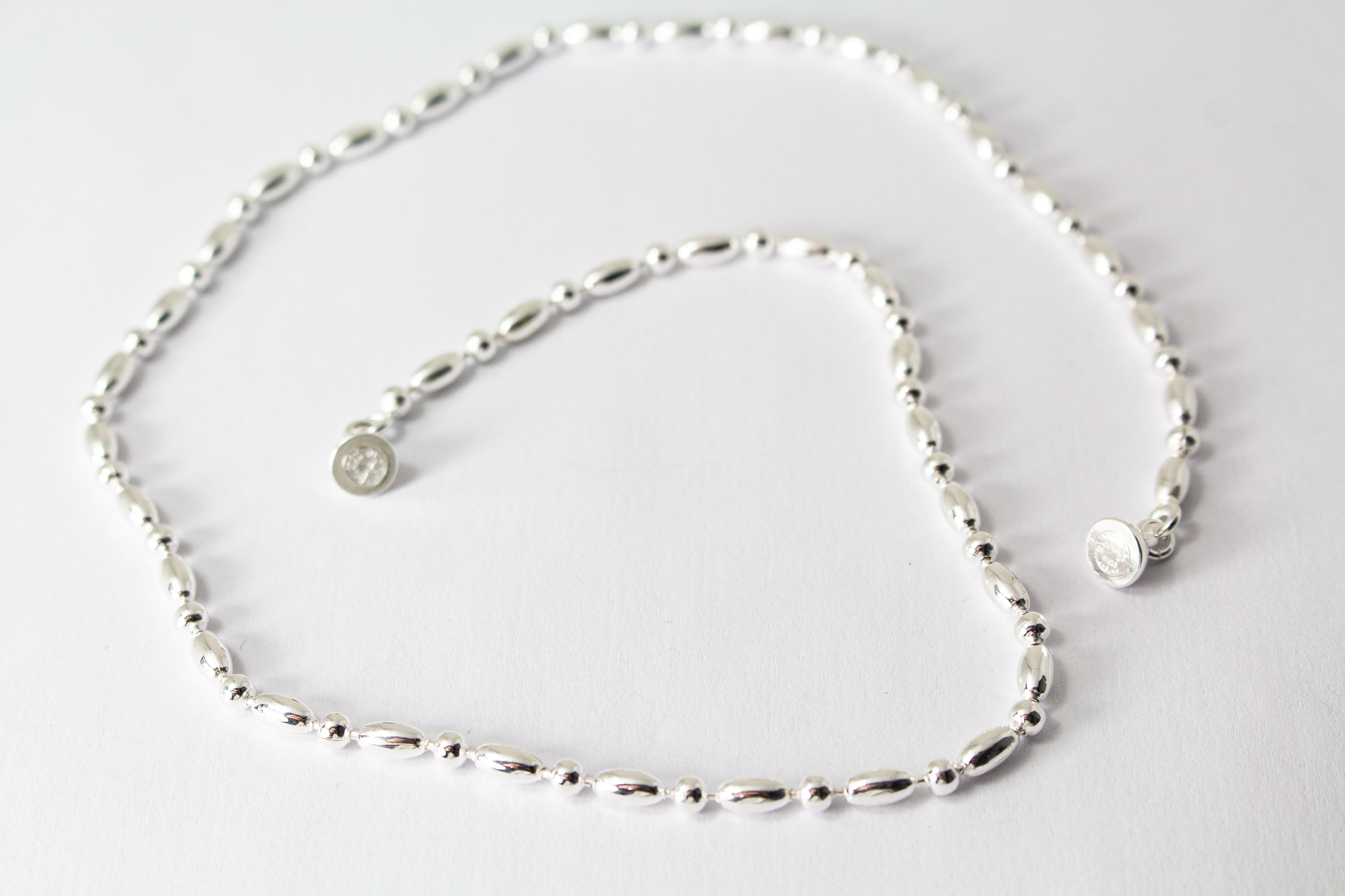 Filigrane Silberkette aus hochglanzpoliertem 925er Sterlingsilber mit einem rhythmischen Wechsel aus Oliven- und Kugel-Elementen auf hellem Untergrund, exklusiv erhältlich im Schmuck-Onlineshop der Goldschmiede Regina Kraus.