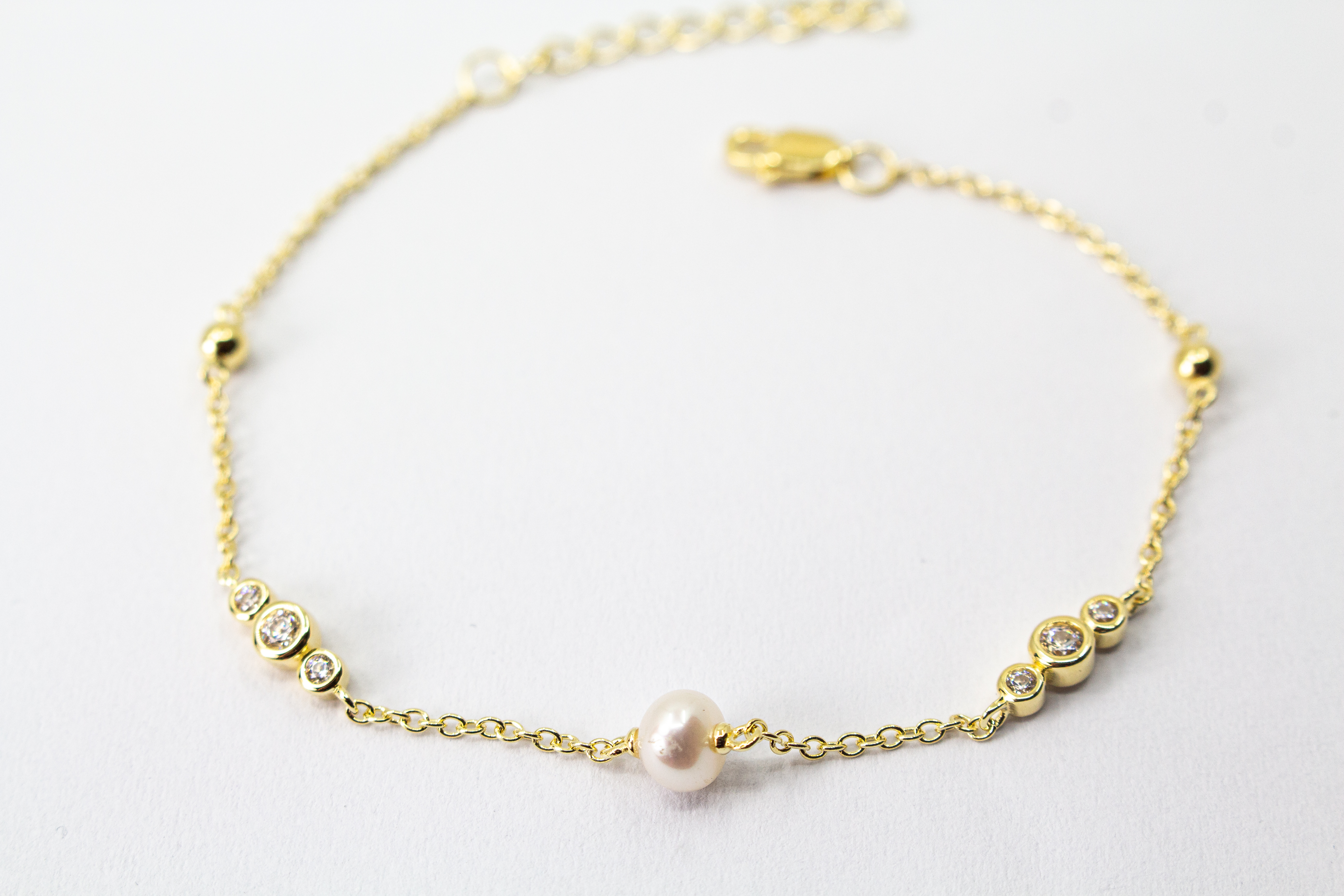 Edles Armband der Goldschmiede Regina Kraus aus vergoldetem 925er Silber mit einer zentralen Süßwasserperle, flankiert von funkelnden Zirkonia-Elementen und kleinen Goldkugeln