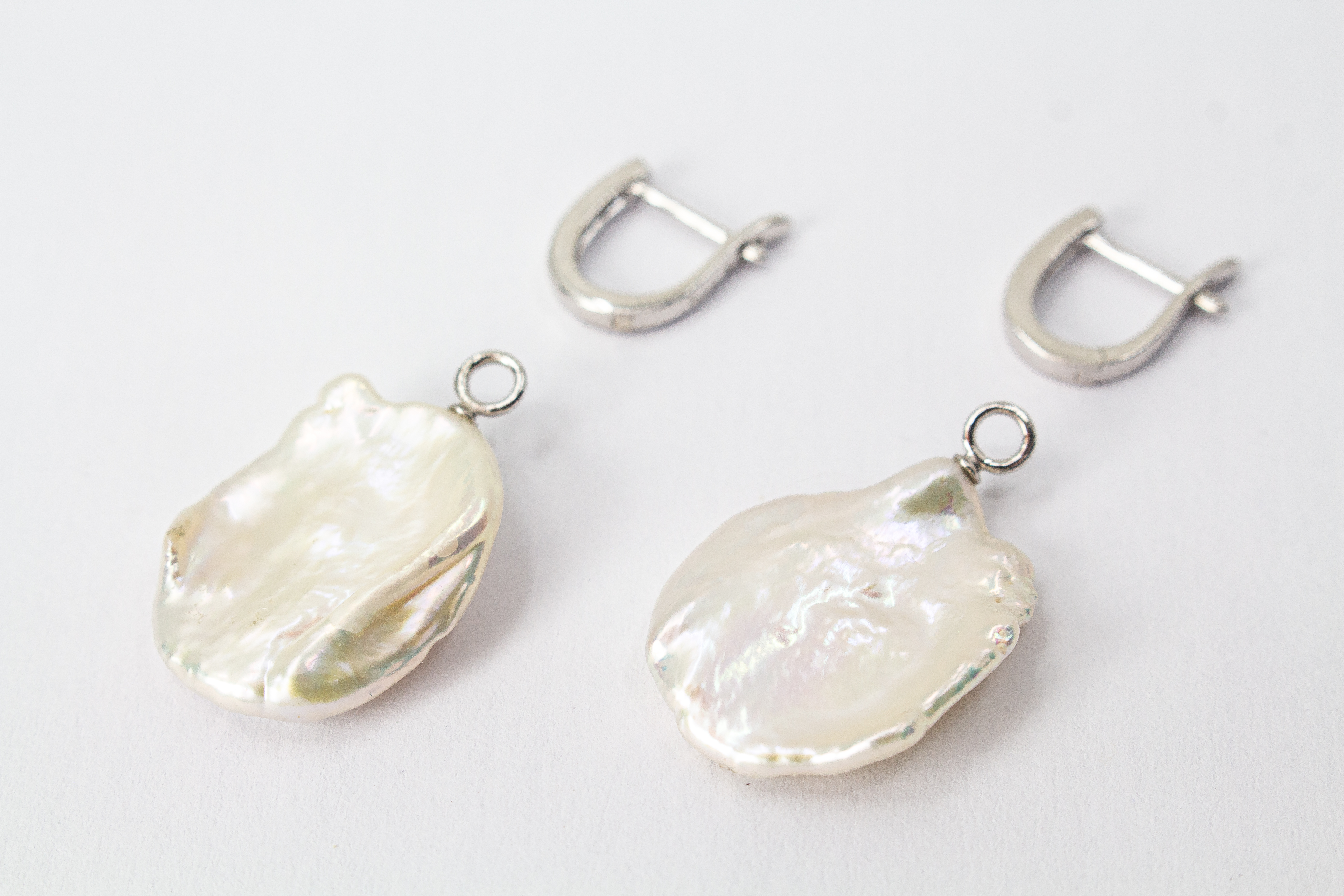 Ein Paar wandelbare Wechselcreolen „Meeresskulptur“ aus rhodiniertem 925er Sterlingsilber von der Goldschmiede Regina Kraus. Die Ohrringe tragen abnehmbare Anhänger aus großen, flachen weißen Keshi-Zuchtperlen, die durch ihre organische Freiform wie eine