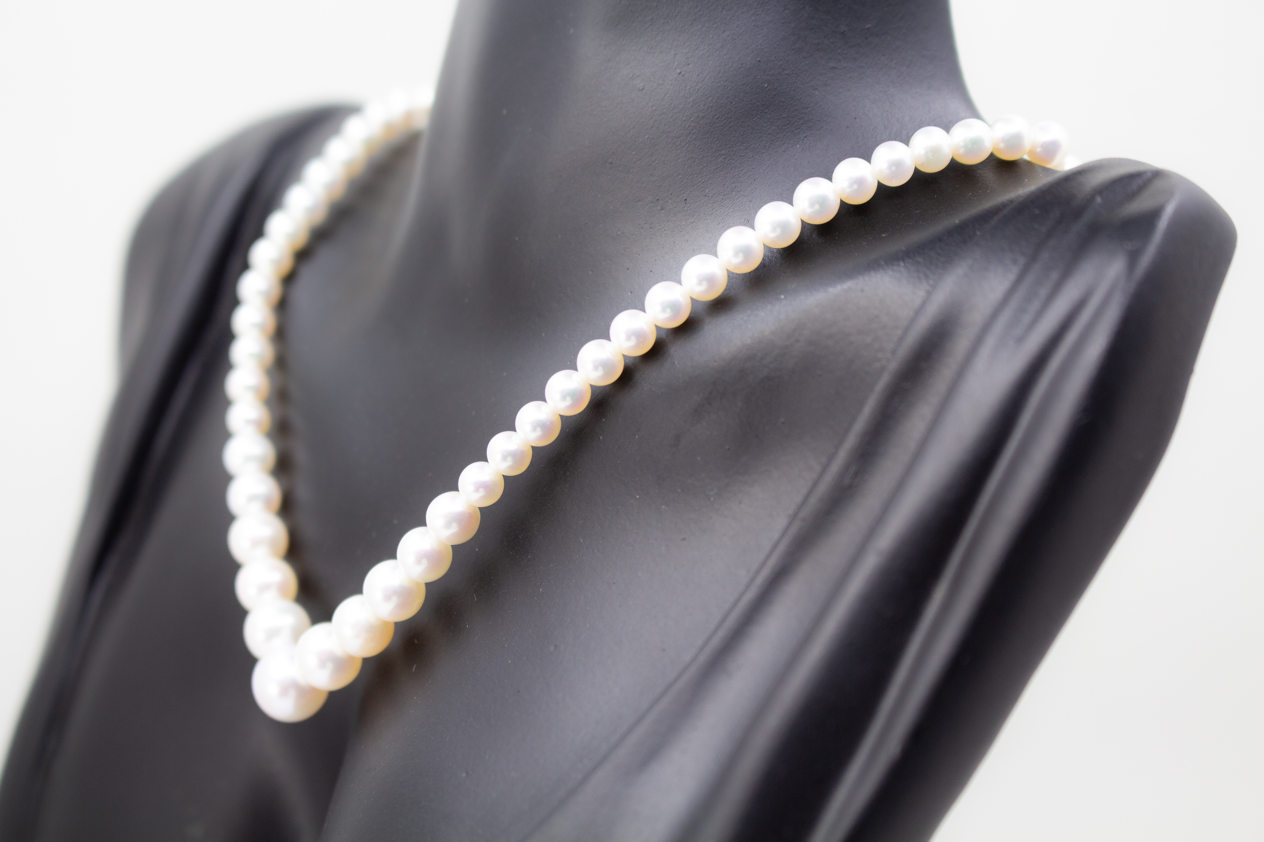 Eine klassische Süßwasserzuchtperlenkette von der Goldschmiede Regina Kraus, elegant geschwungen auf weißem Hintergrund ausgelegt. Die runden Perlen weisen einen zarten, cremeweißen Lüster auf und sind im harmonischen Verlauf angeordnet, wobei die größte