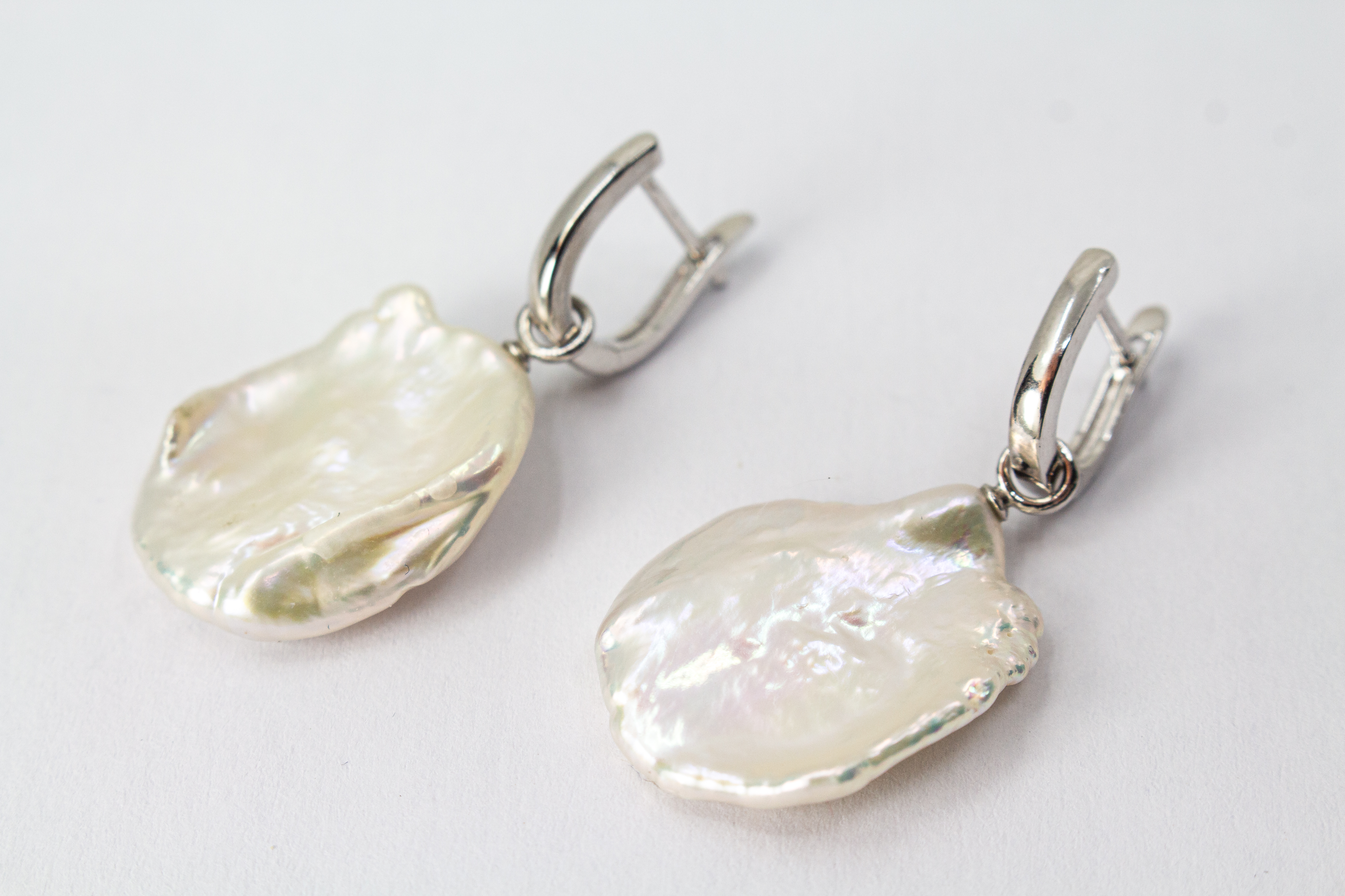 Ein Paar wandelbare Wechselcreolen „Meeresskulptur“ aus rhodiniertem 925er Sterlingsilber von der Goldschmiede Regina Kraus. Die Ohrringe tragen abnehmbare Anhänger aus großen, flachen weißen Keshi-Zuchtperlen, die durch ihre organische Freiform wie eine