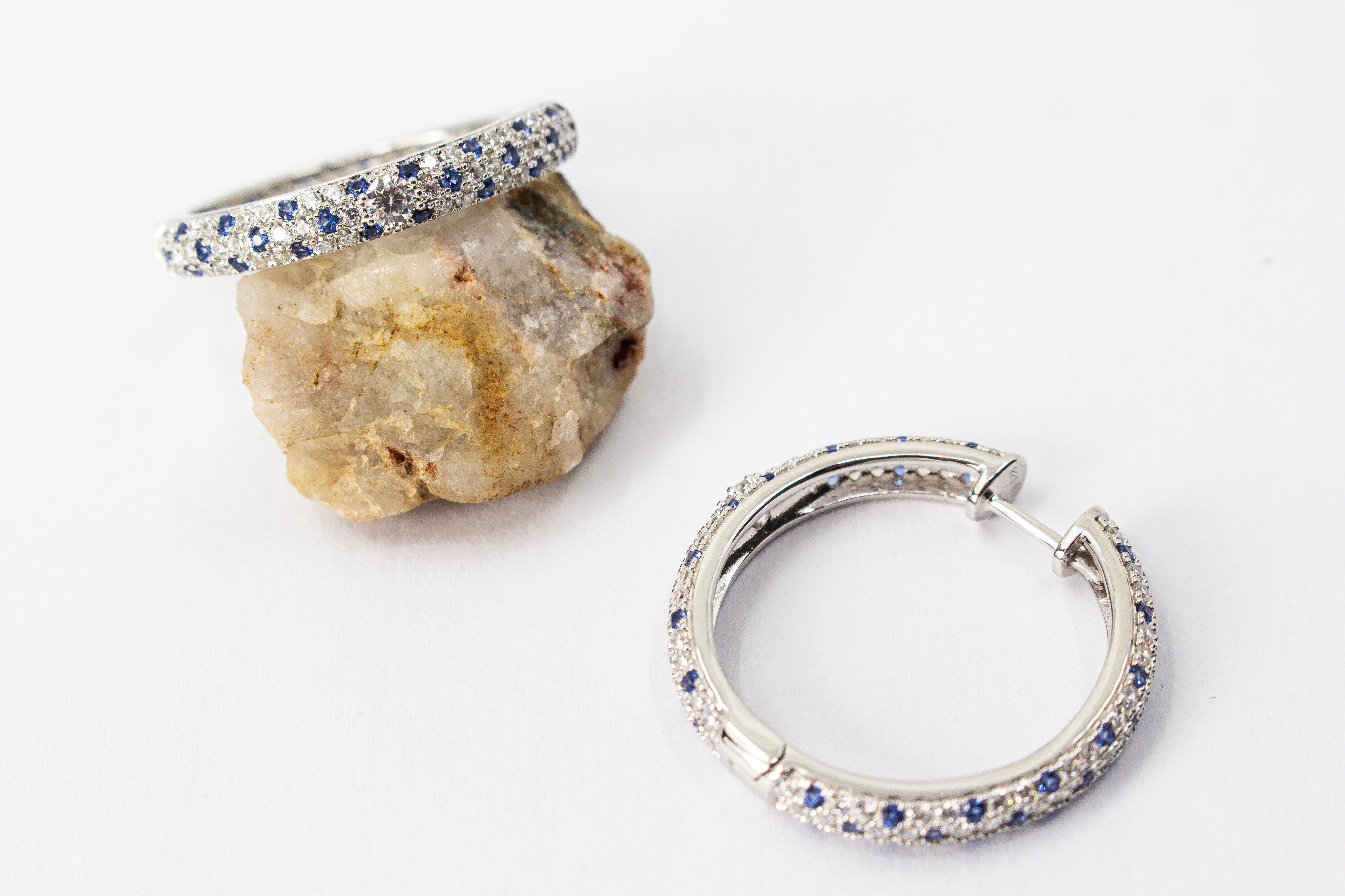 Ein Paar luxuriöse, rhodinierte Klappcreolen aus 925er Sterlingsilber von der Goldschmiede Regina Kraus. Die breite Außenseite ist dreireihig im edlen Pavé-Stil mit funkelnden, weißen und saphirblauen Zirkonia-Steinen besetzt. Eine Creole lehnt dekorativ