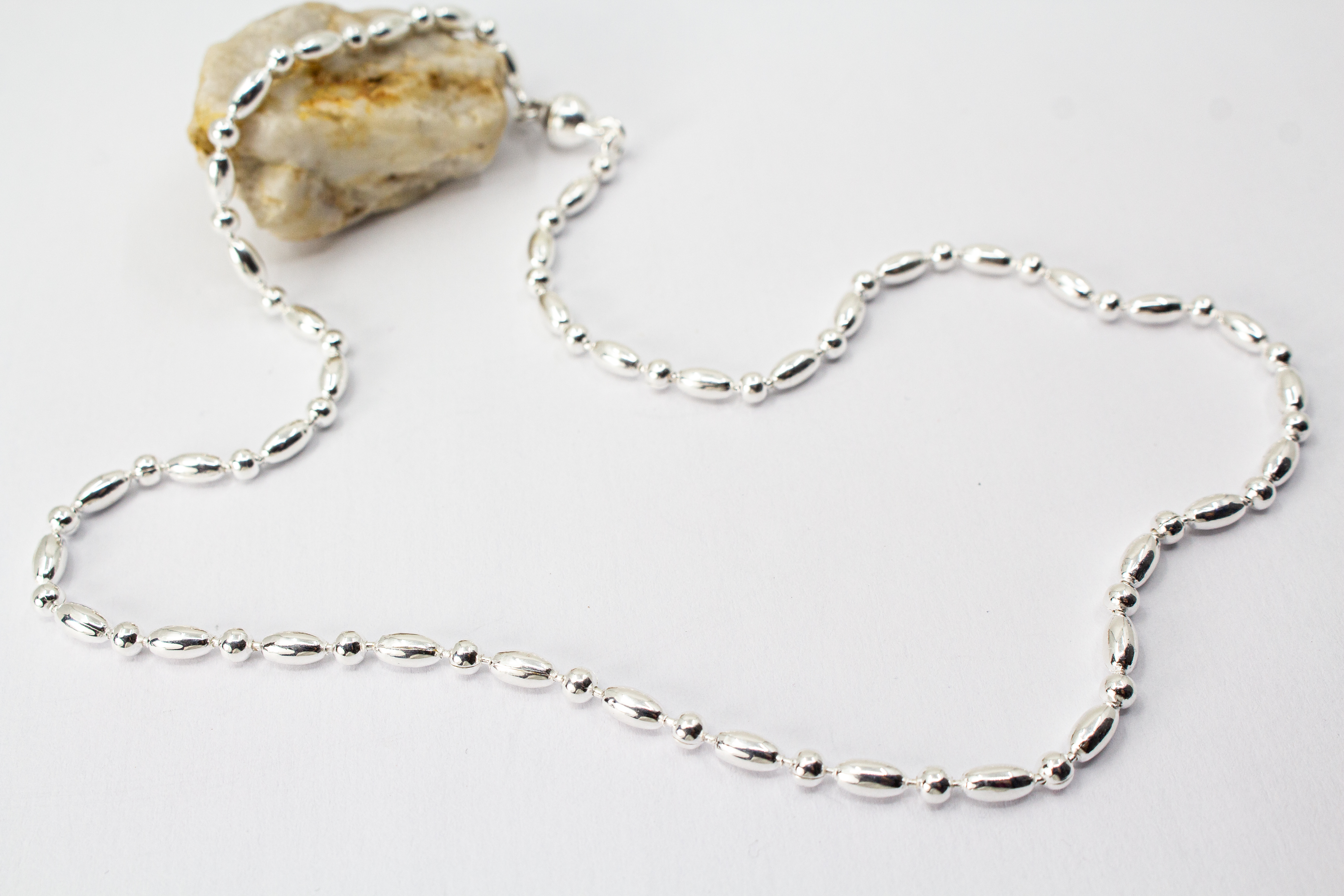 Filigrane Silberkette aus hochglanzpoliertem 925er Sterlingsilber mit einem rhythmischen Wechsel aus Oliven- und Kugel-Elementen auf hellem Untergrund, exklusiv erhältlich im Schmuck-Onlineshop der Goldschmiede Regina Kraus.