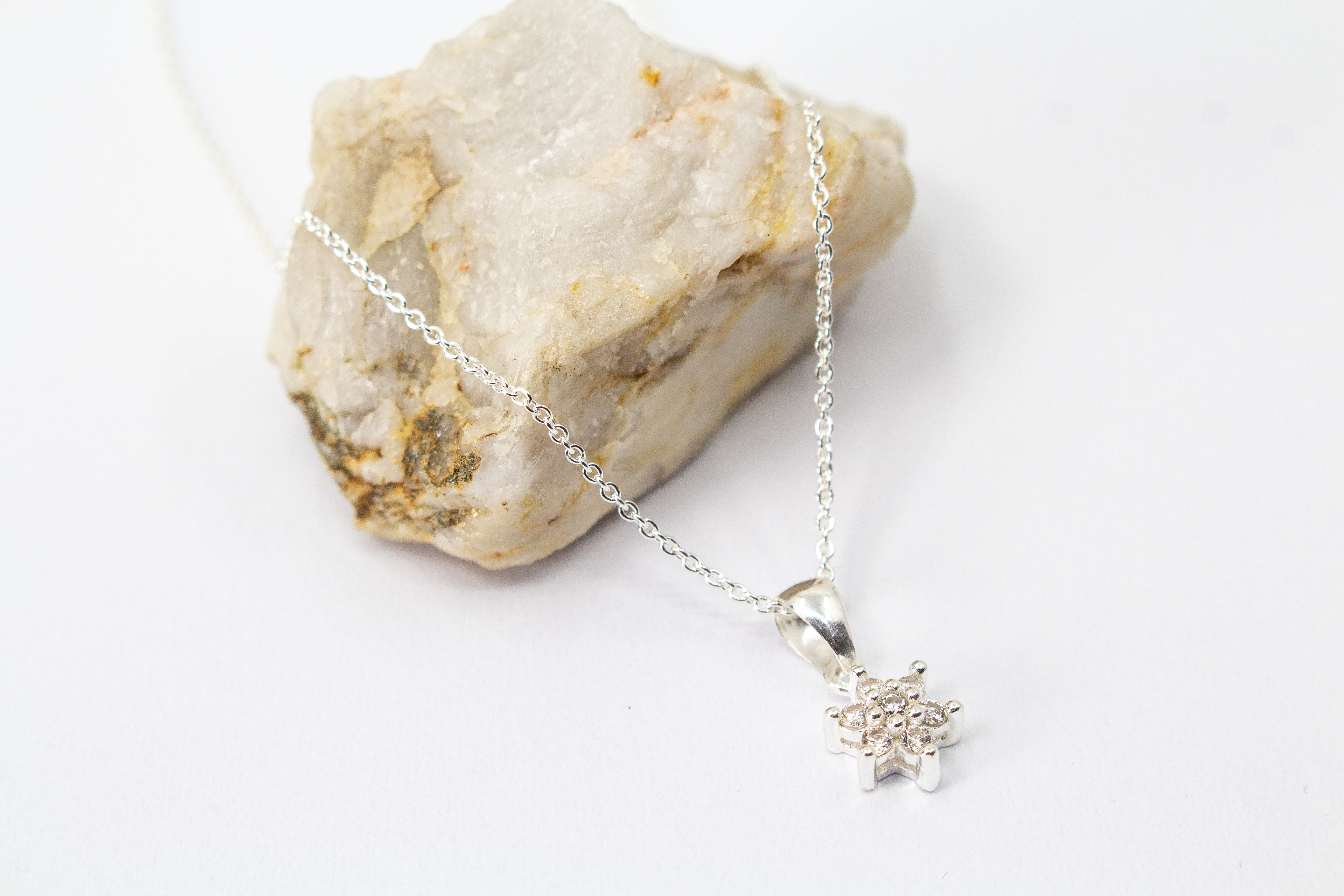 Filigrane Halskette aus 925er Sterling-Silber mit einem stern- oder blütenförmigen Anhänger, der mit funkelnden Zirkonia-Kristallen besetzt ist, präsentiert auf einem hellen Naturstein – exklusiver Schmuck von der Goldschmiede Regina Kraus.