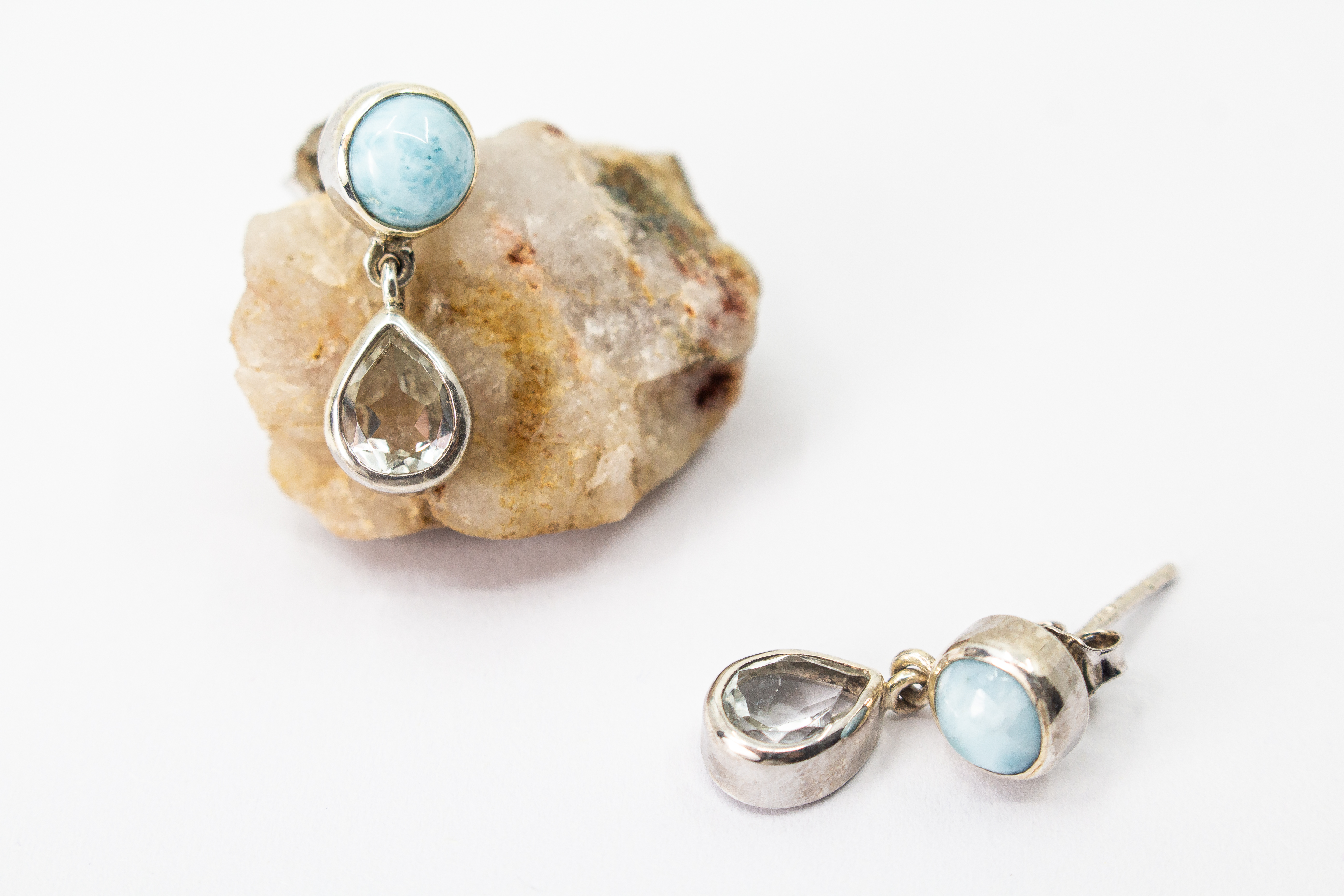 Filigrane, zweiteilige Ohrstecker aus 925 Sterling Silber mit einer runden, hellblauen Larimar-Kugel und einem frei beweglich hängenden, klaren Bergkristall-Tropfen im Onlineshop der Goldschmiede Regina Kraus.