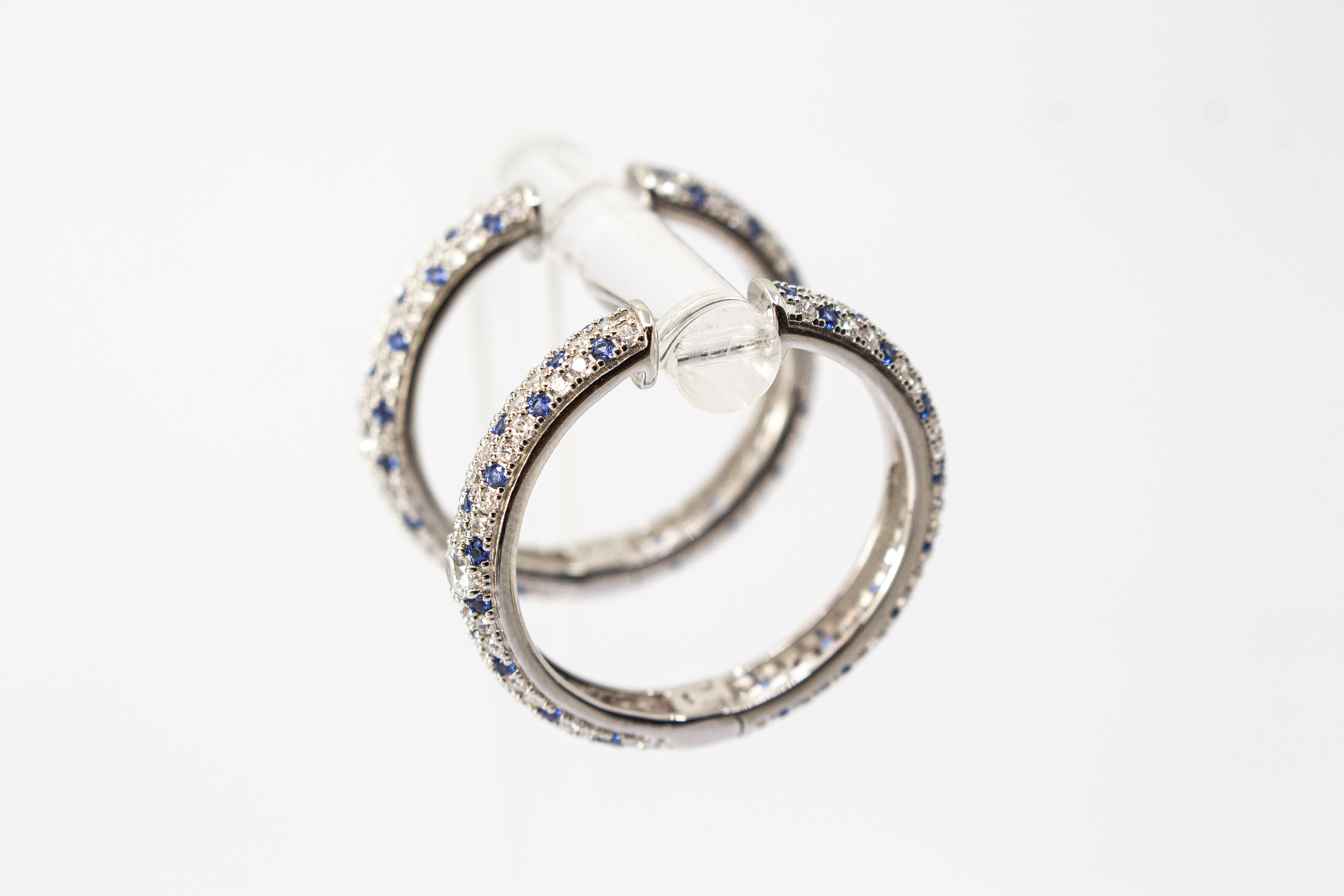 Ein Paar luxuriöse, rhodinierte Klappcreolen aus 925er Sterlingsilber von der Goldschmiede Regina Kraus. Die breite Außenseite ist dreireihig im edlen Pavé-Stil mit funkelnden, weißen und saphirblauen Zirkonia-Steinen besetzt. Eine Creole lehnt dekorativ