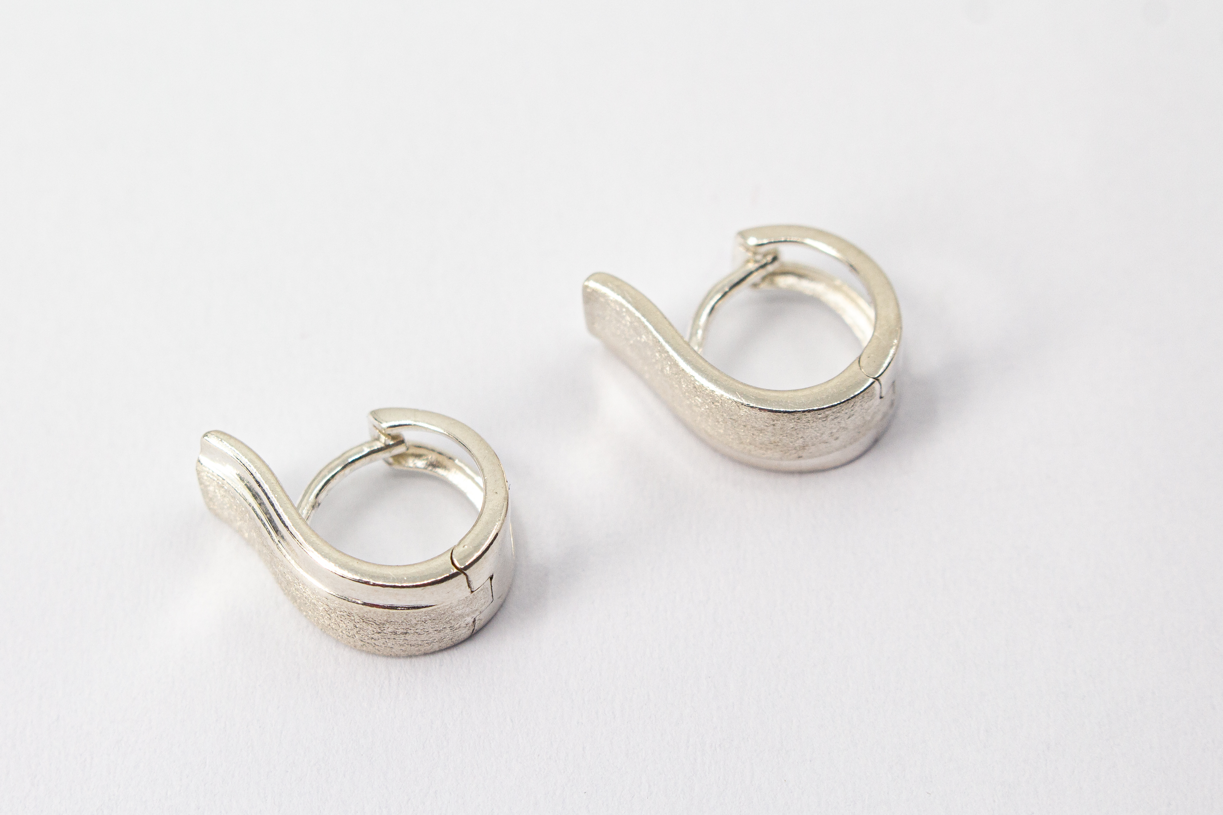 Breite Klappcreolen aus 925er Silber mit einer schwungvoll hochgezogenen, eismattierten Vorderseite und glänzend polierten Kanten im Onlineshop von Goldschmiede Regina Kraus.