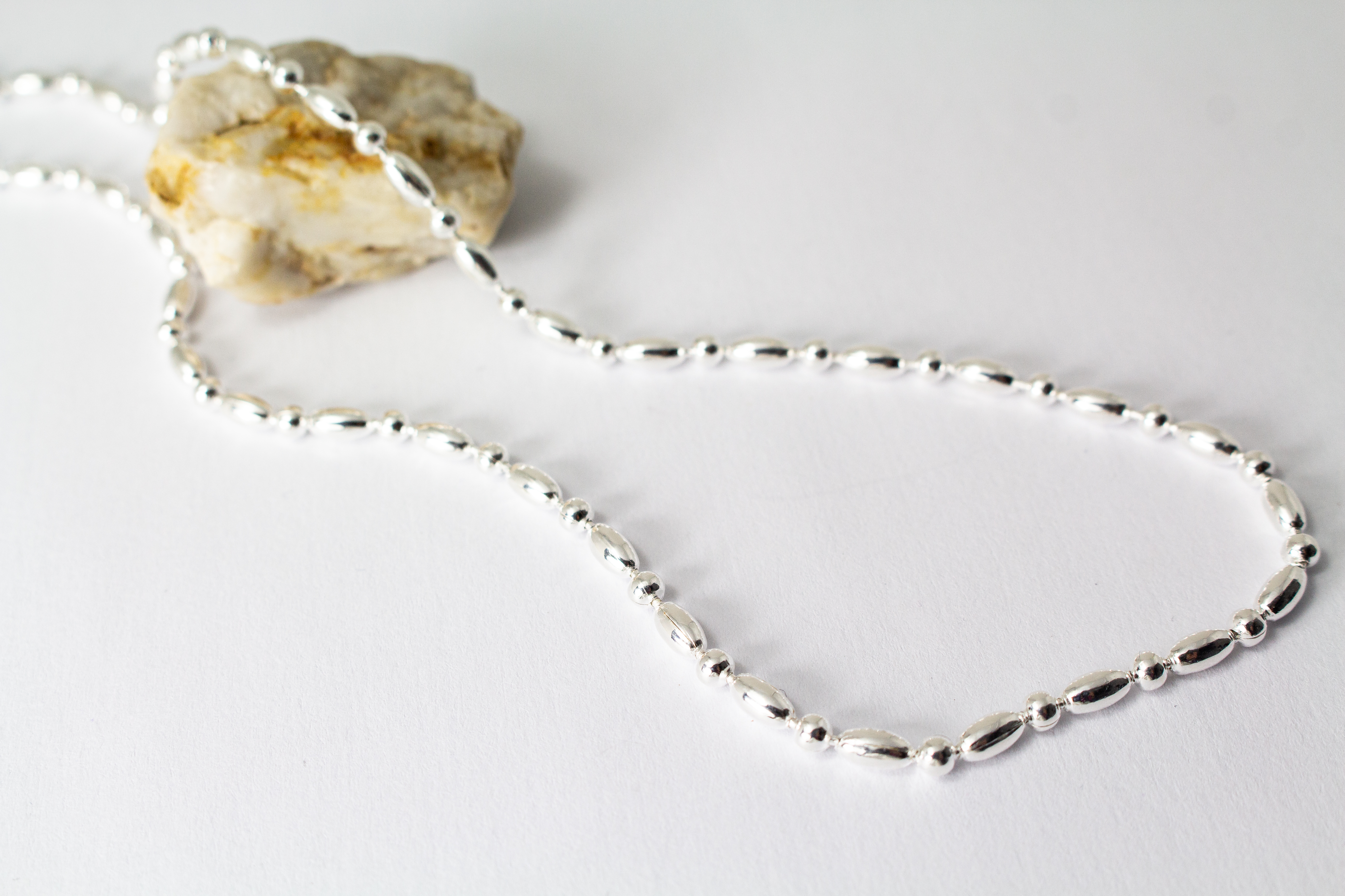Filigrane Silberkette aus hochglanzpoliertem 925er Sterlingsilber mit einem rhythmischen Wechsel aus Oliven- und Kugel-Elementen auf hellem Untergrund, exklusiv erhältlich im Schmuck-Onlineshop der Goldschmiede Regina Kraus.